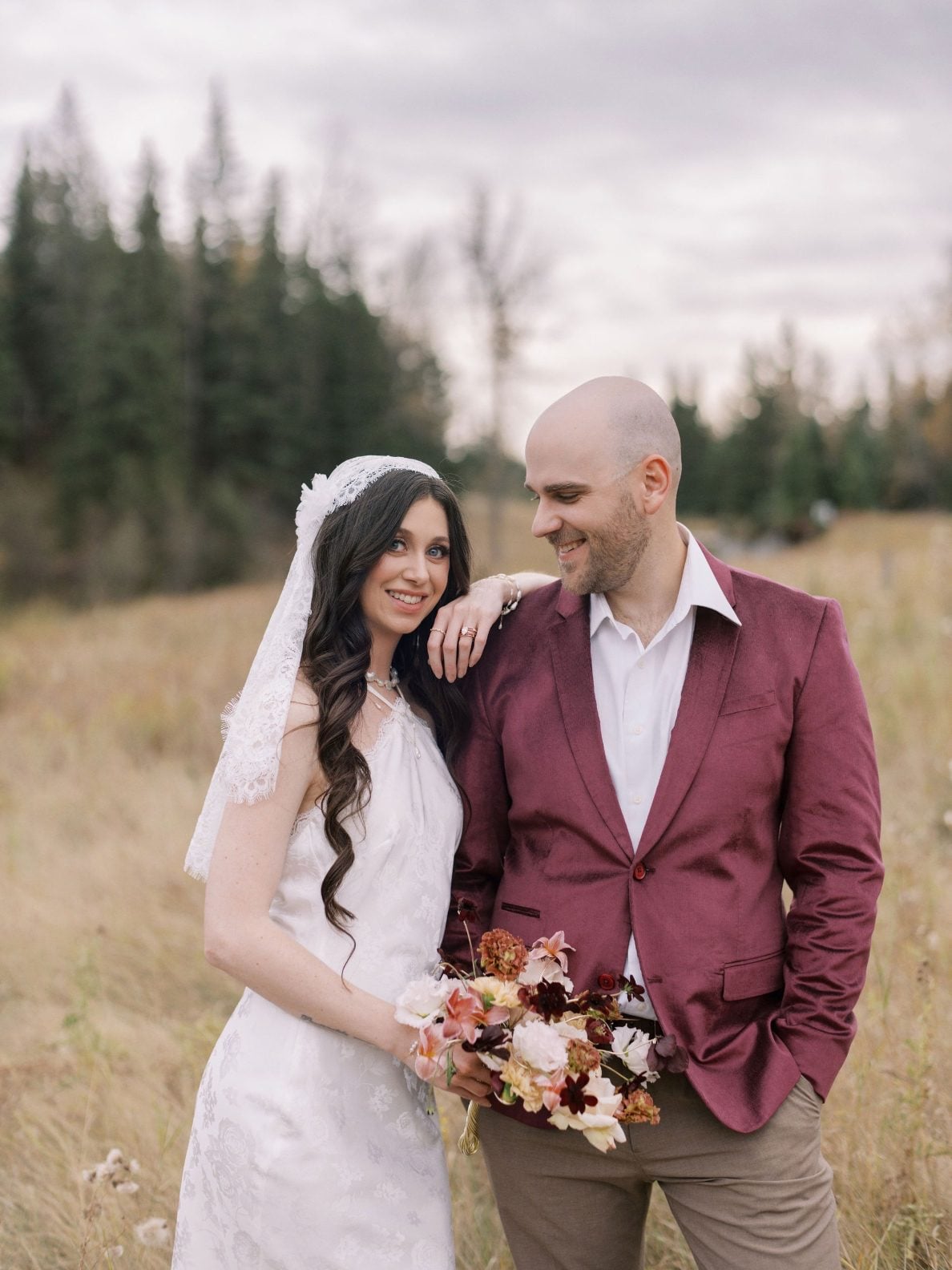 Justine Milton Marsala Couple in Meadow True to Hue Marsala photoshoot, model couple stands in grassy meadow while the bride holds a bouquet of blush and burgundy.