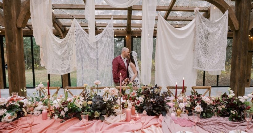 Justine Milton True to Hue FT Couple shares a kiss behind Marsala inspired table scape for this True to Hue photoshoot amongst lace and gauzy fabrics draping from the ceiling.