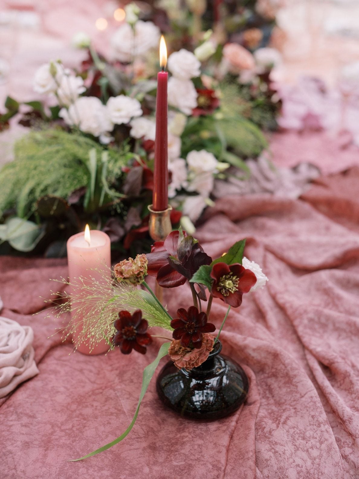 Justine Milton True to Hue Hellebore Budvase and Centrepiece A black glass bud vase with hellebores next to various candles and large marsala inspired centrepiece running down the length of the table.