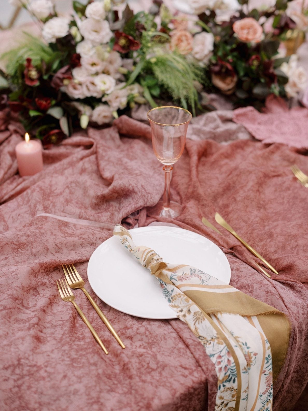 Justine Milton True to Hue Table Linens Stunning patterned napkin on top of a simple white plate for this place setting, accented with gold flatware and gold accented glassware at this gorgeous marsala inspired True to Hue table scape.