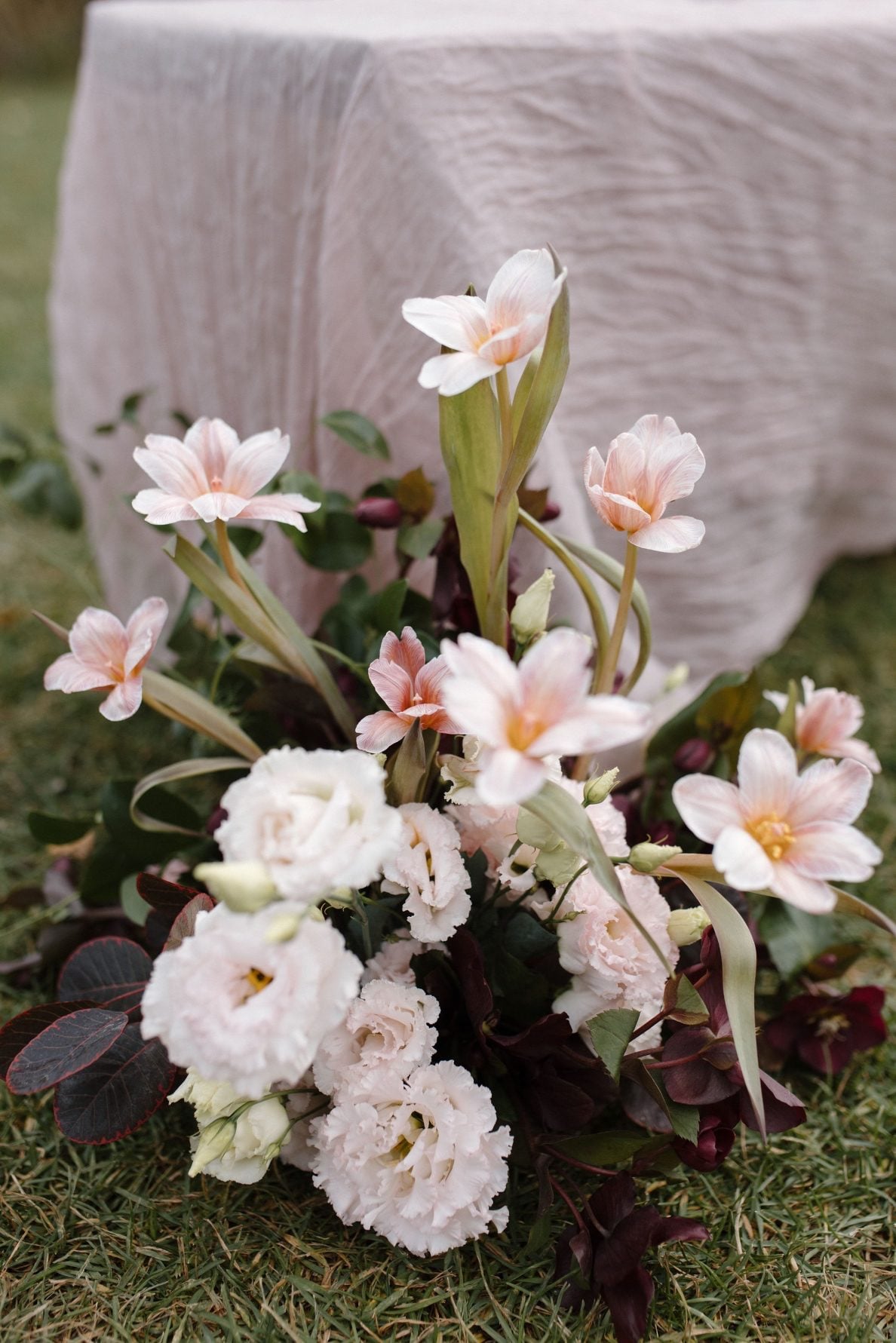 Nikki Collette Marsala Aisle Arrangements Aisle arrangements for the True to Hue photoshoot with reflexed tulips, lisianthus, hellebores, smokebush and ruscus next to pale blush gauzy fabric draped over the benches.