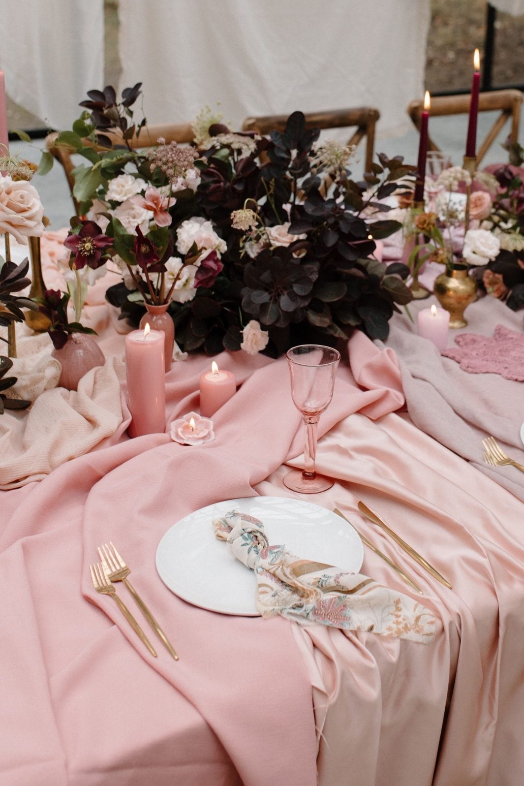 Nikki Collette Marsala Tablescape Close up of beautifully styled place setting of this marsala inspired table scape, showing pink candles nestled among soft drapey fabric and lush floral centrepiece.
