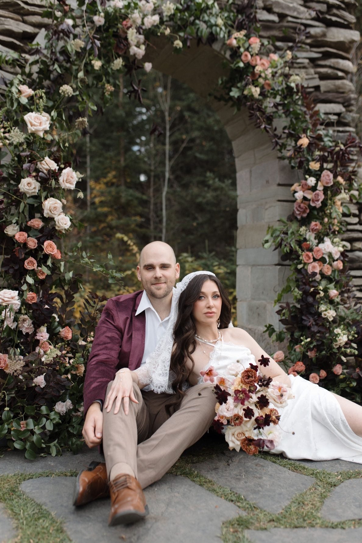 Nikki Collette Marsala True to Hue Couple at Ceremony Model bride and groom sit next to the ceremony flowers adorning the stone arch at The Valley.