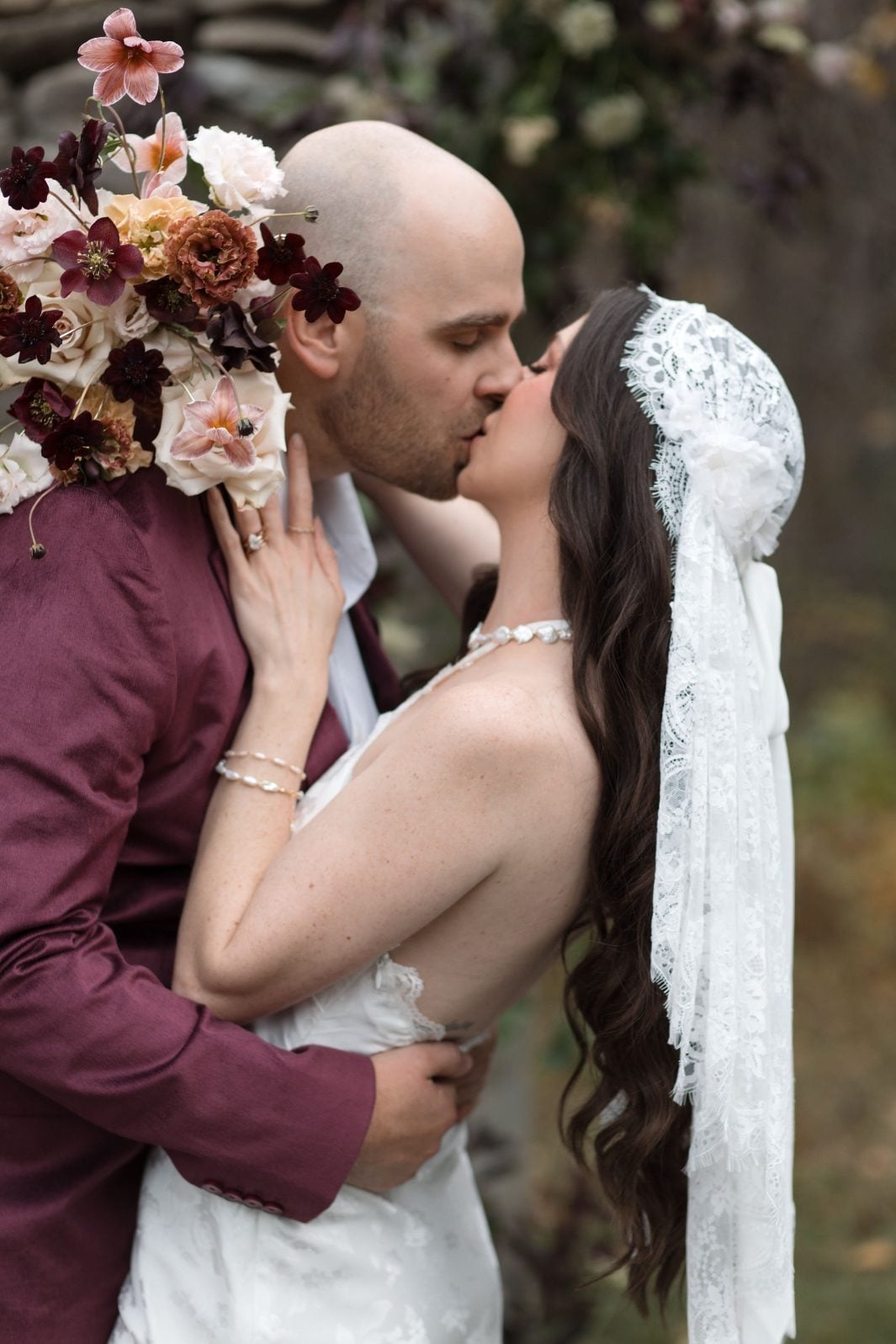 Nikki Collette True to Hue Marsala Couple Bride holds her gorgeous blush and burgundy bridal bouquet with her arm wrapped around the grooms neck as they share a kiss for this marsala True to Hue Photoshoot by Bronte Bride.