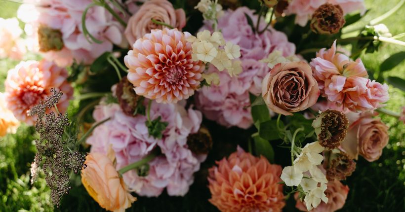 Colourful ceremony arrangement in a mixture of oranges and pinks including peaches and cream dahlias, pink hydrangea, cappuccino roses, chocolate lace, mocha lisianthus and phlox.