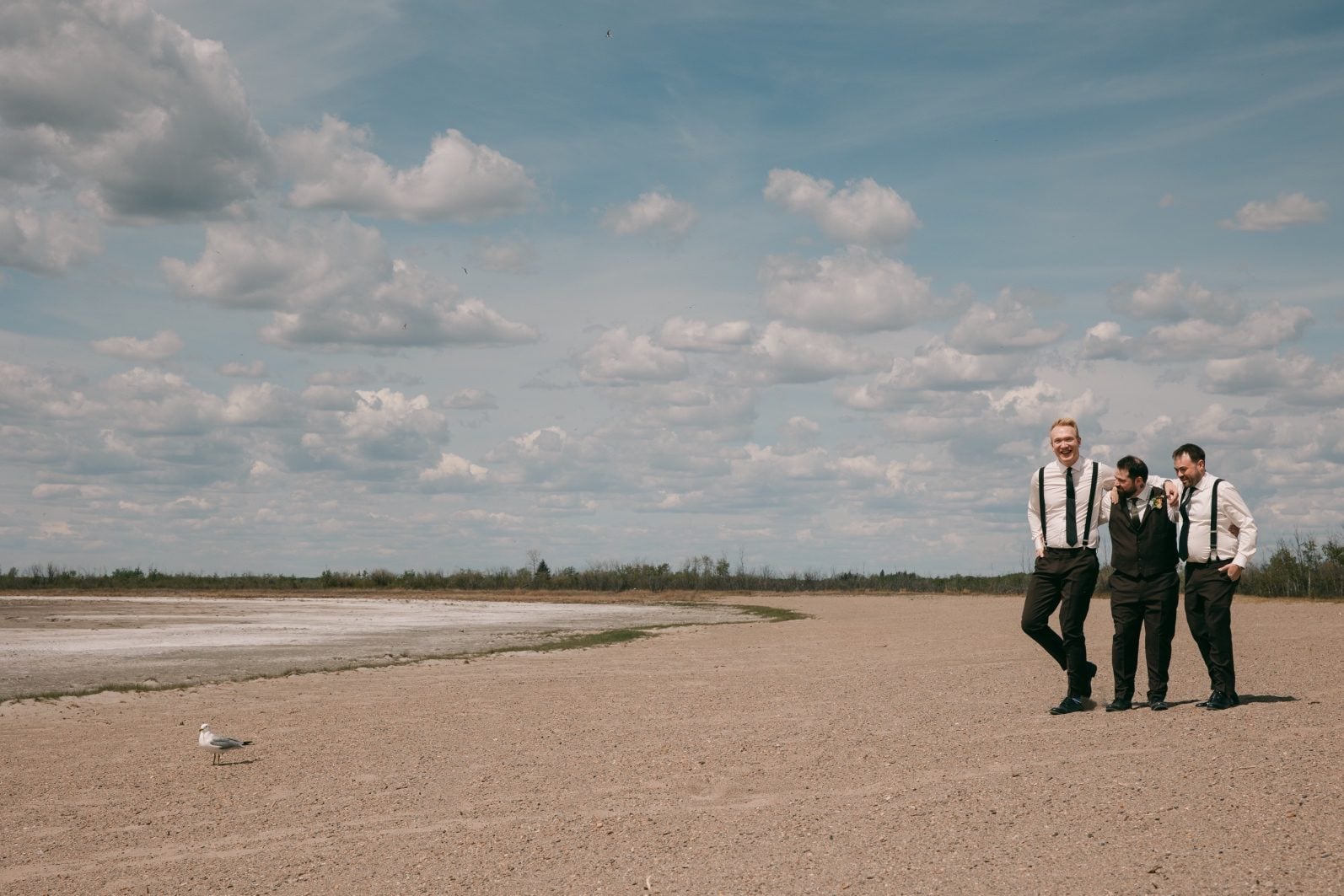 Groom and groomsmen sharing a candid moment beneath a blue Alberta sky on the wedding day at Buffalo Lake.