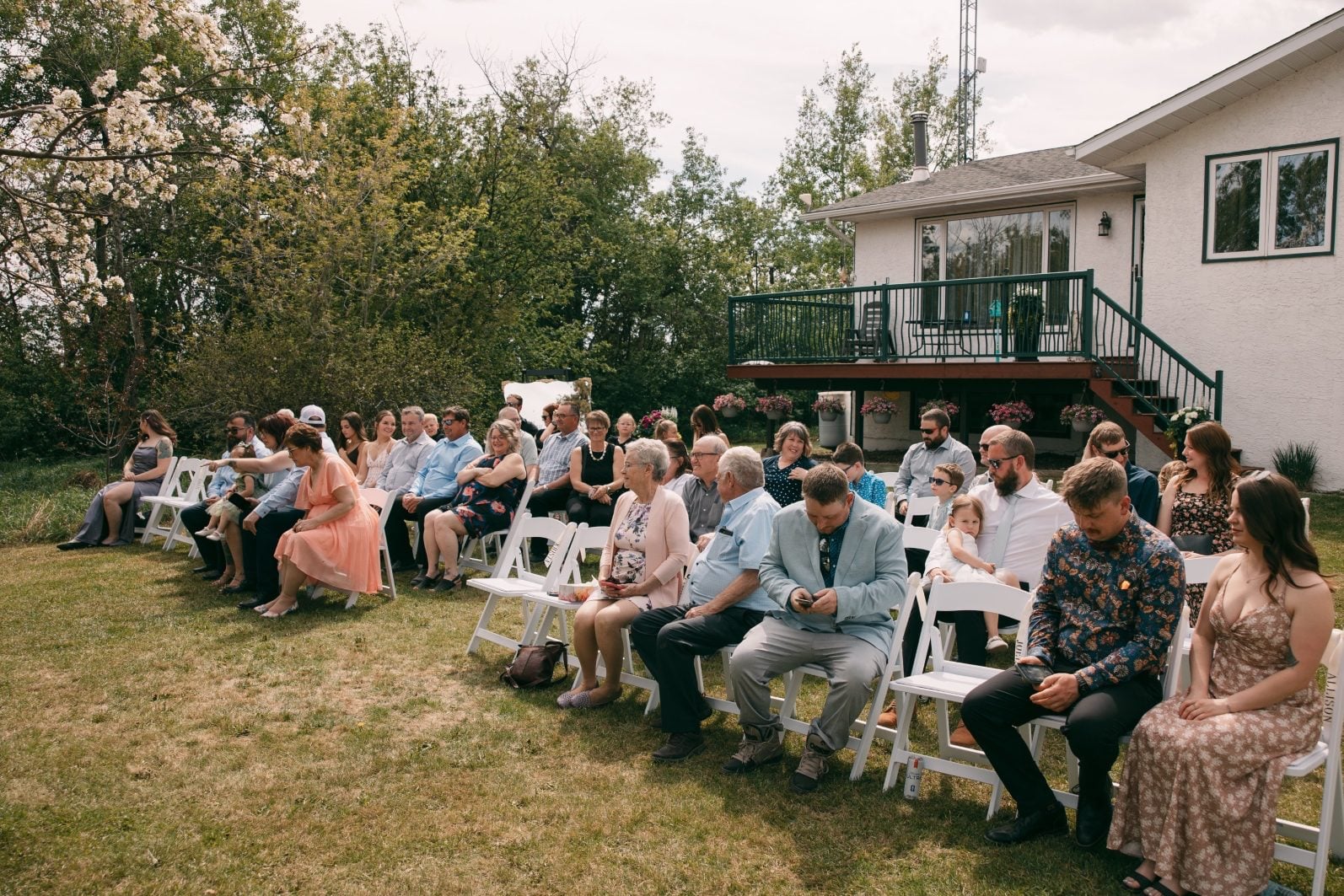 Wedding guests seated on white chairs for an intimate outdoor spring ceremony surrounded by trees.