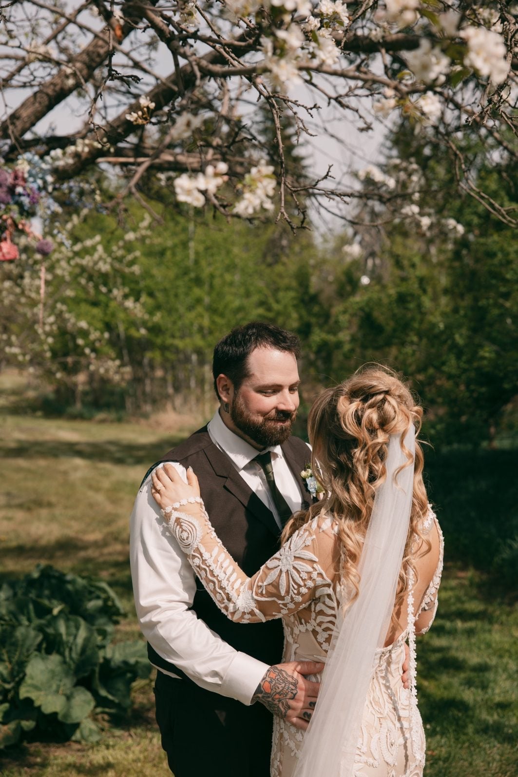 Bride and groom embracing beneath the blooming branches of a tree at their intimate outdoor wedding ceremony.