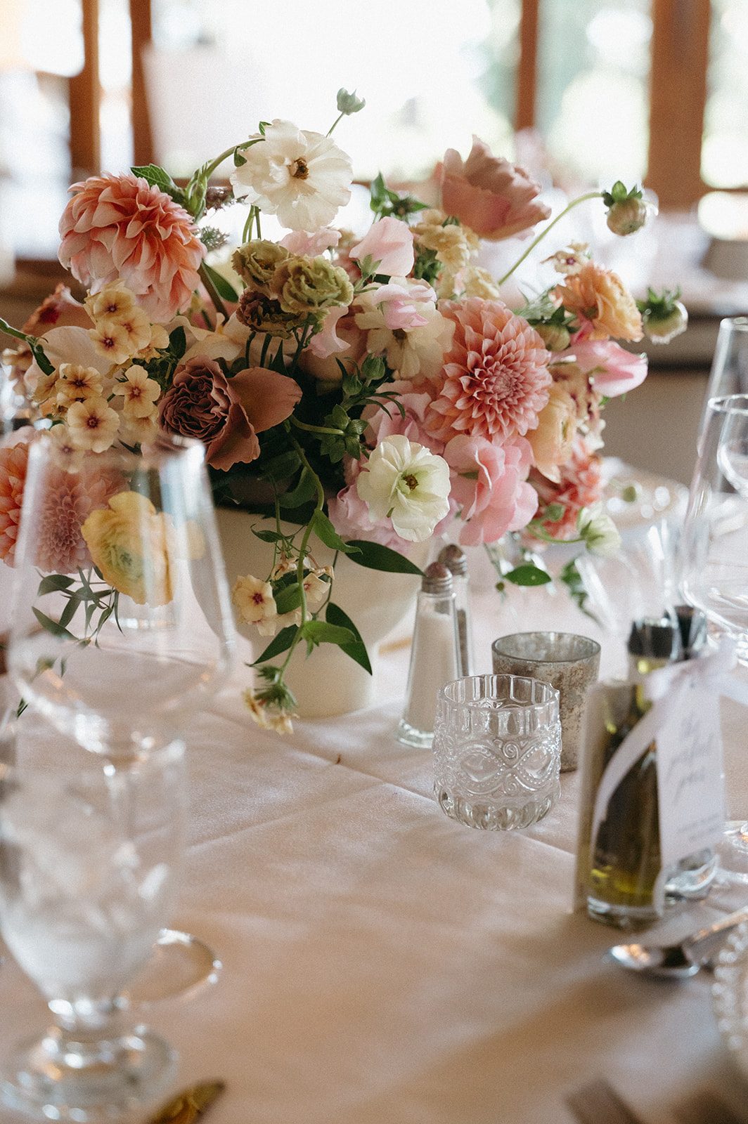 Centrepiece on guest tables at pink and peach wedding reception full of garden inspired blooms.