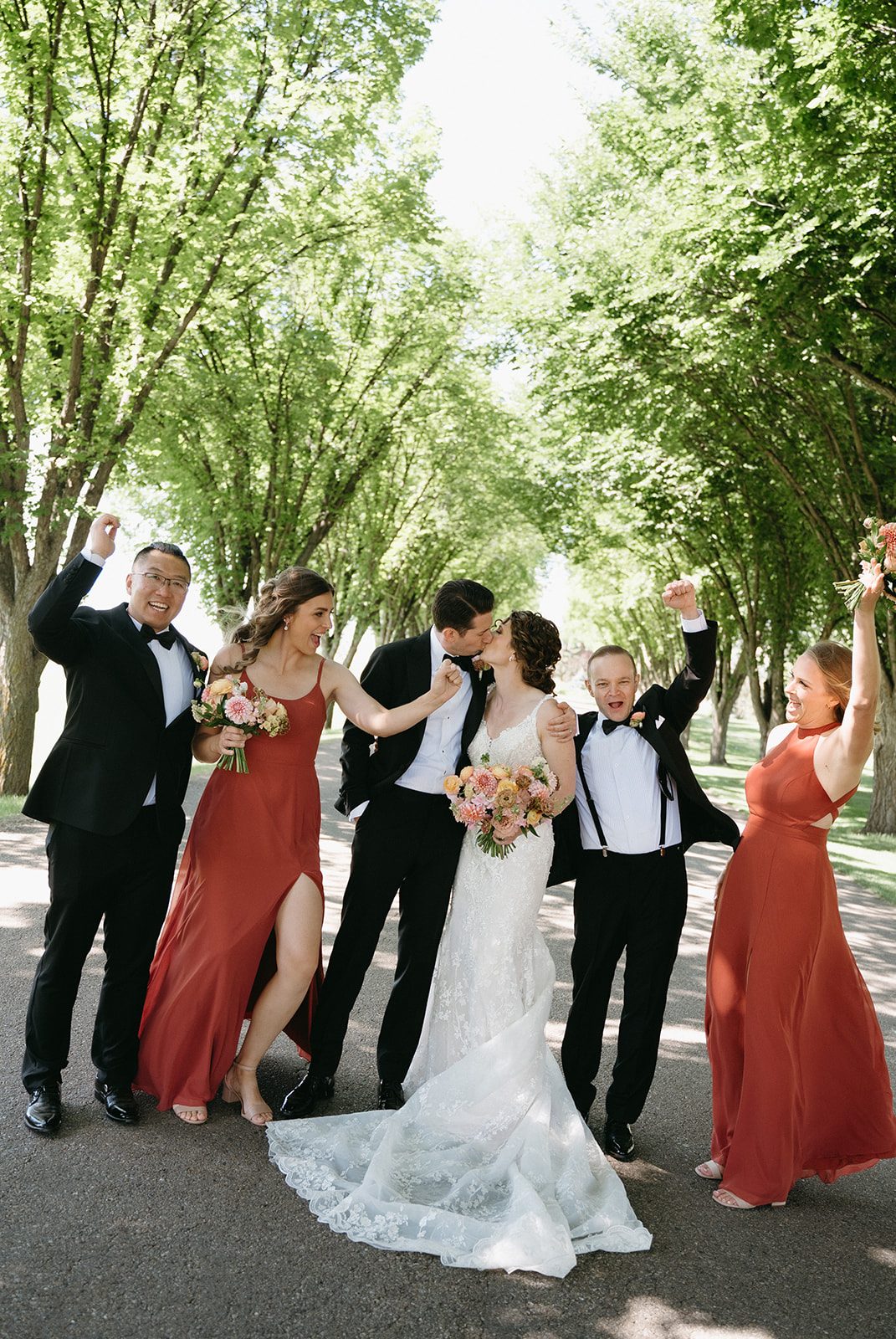 Bride and groom share a kiss while their wedding party surround them cheering.