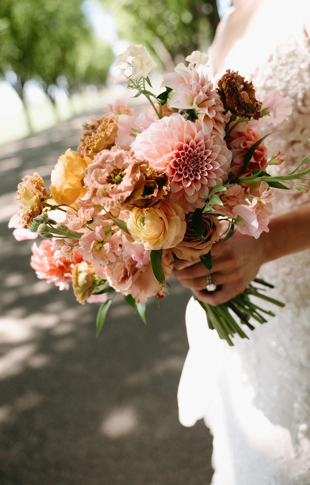 Close up of brides pink and peach bridal bouquet featuring garden inspired blooms including dahlias, ranunculus, roses, lisianthus, stock, and phlox.