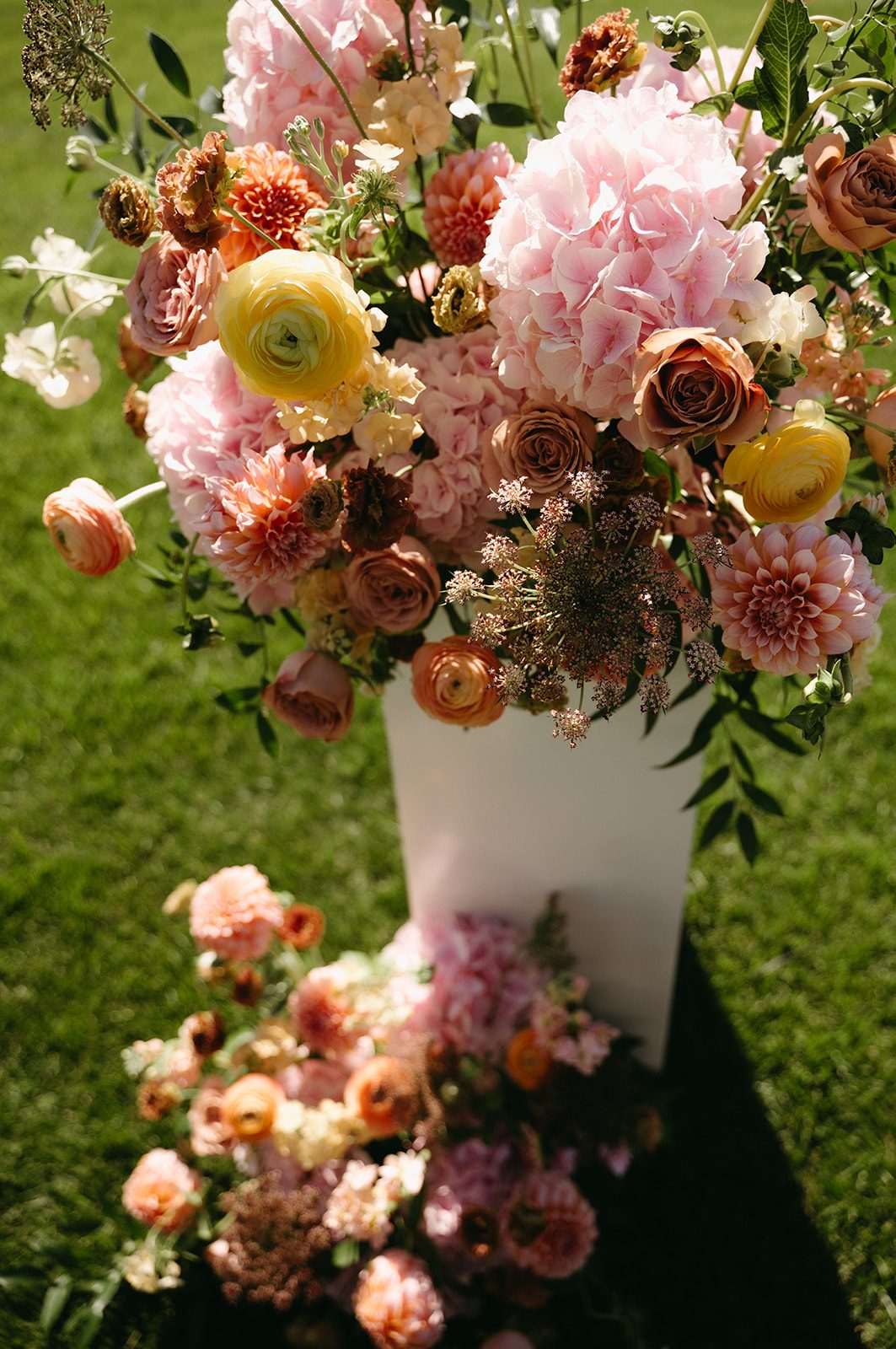 Pink and peach pillar arrangement featuring garden inspired blooms including hydrangea, dahlias, roses, ranunculus, phlox, chocolate lace and stock.