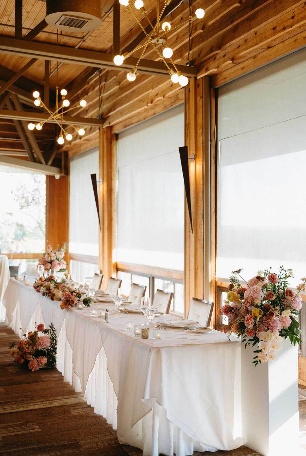 Elegant head table at Pinebrook Golf & Country Club reception, adorned with several pink and peach arrangements.