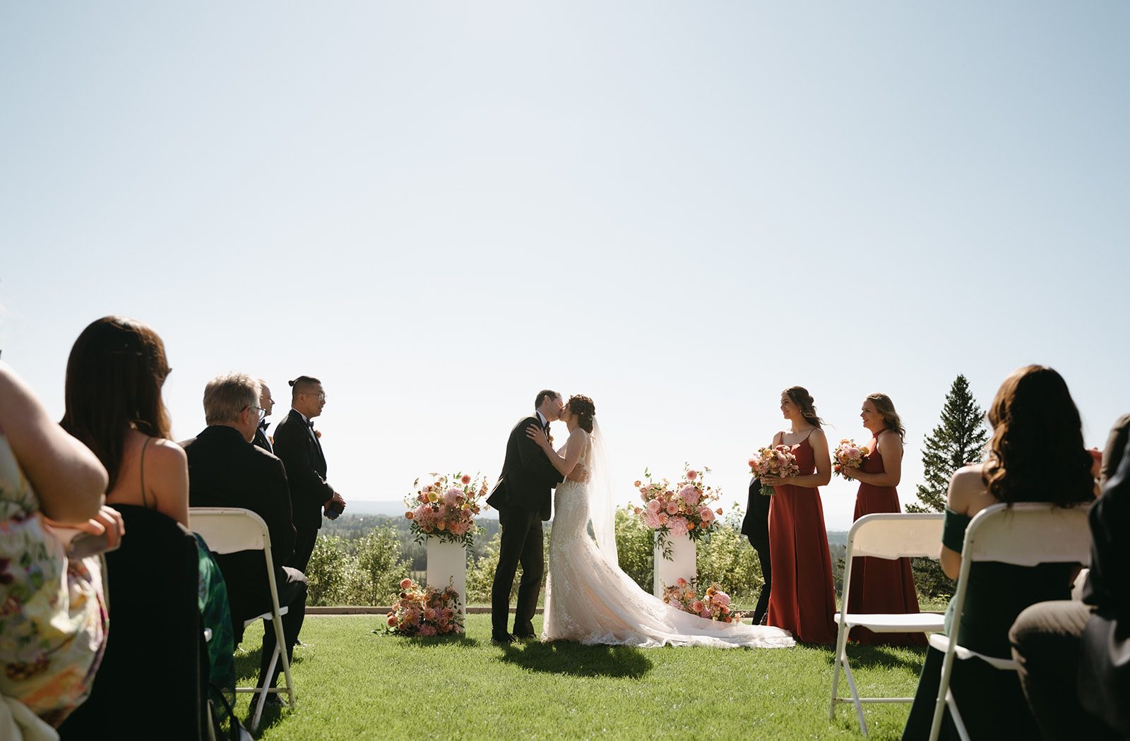Bride and groom share a kiss to make it official during their ceremony, framed by their big pink and peach pillar arrangements.