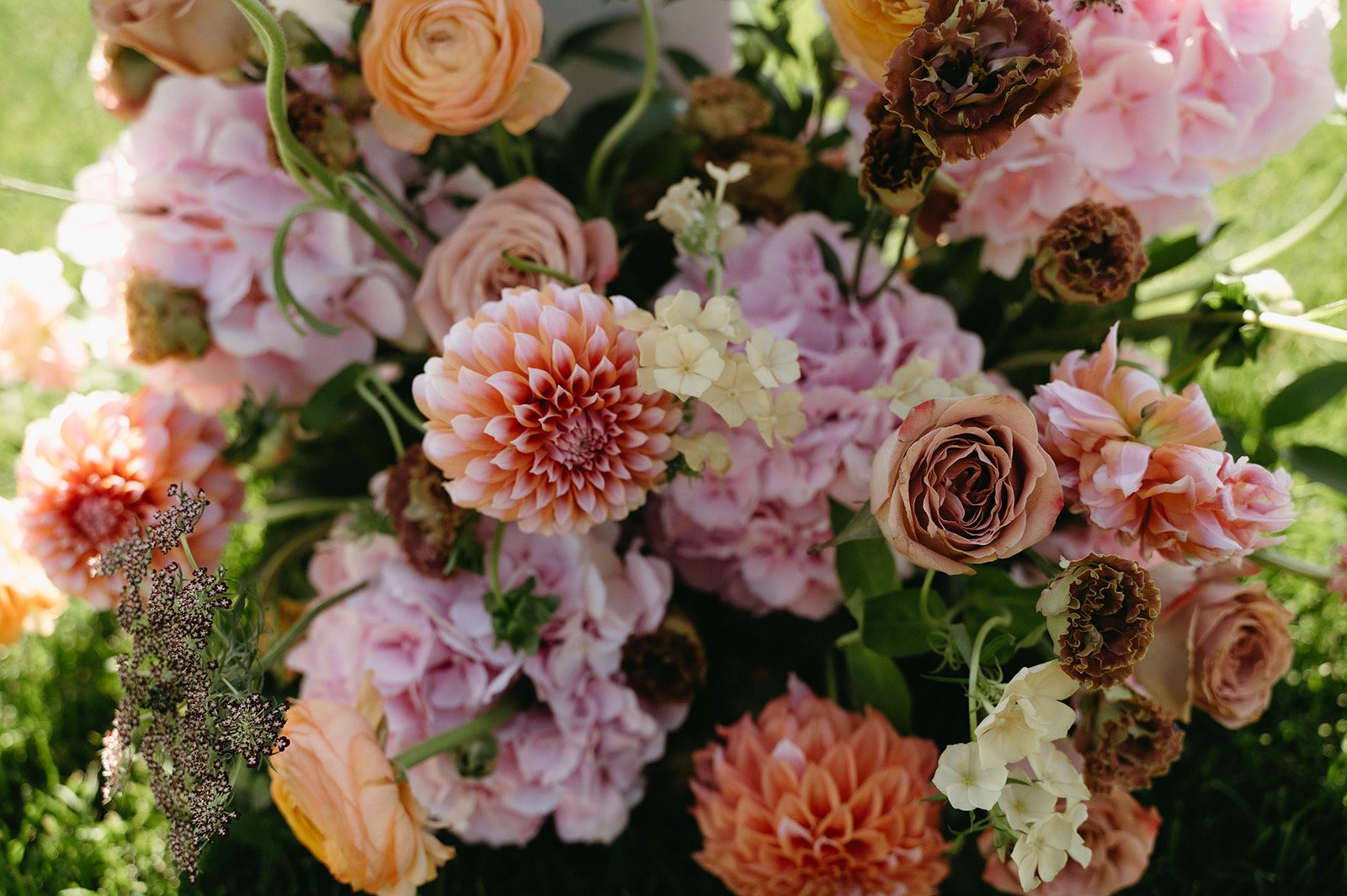 Close up of pink and peach pillar arrangements of hydrangea, dahlias, roses, ranunculus, lisianthus, chocolate lace, phlox and stock.