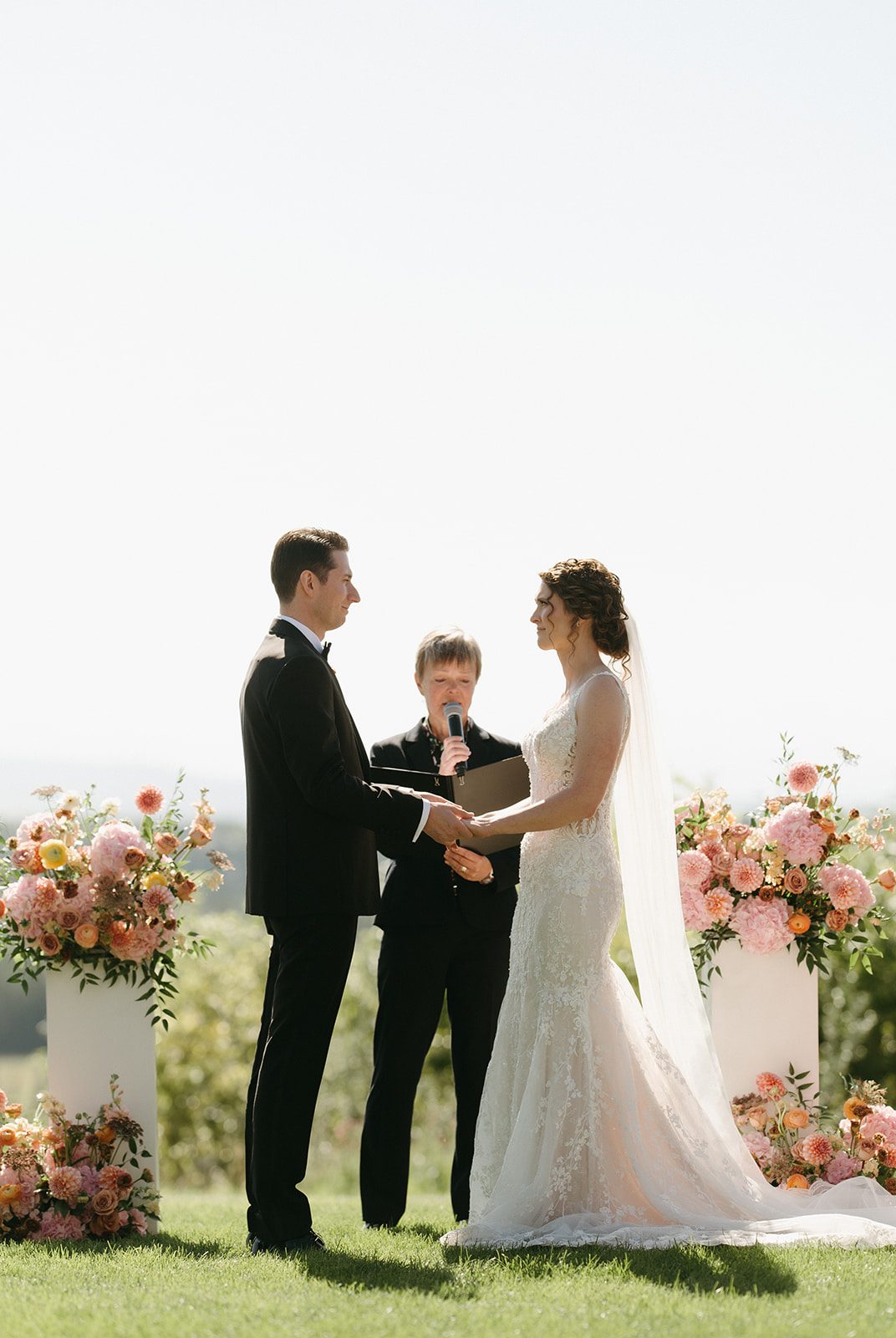 Bride and groom with hands clasped and looking at each other lovingly during this pretty, garden inspired pink and peach wedding ceremony at Pinebook Golf & Country Club.