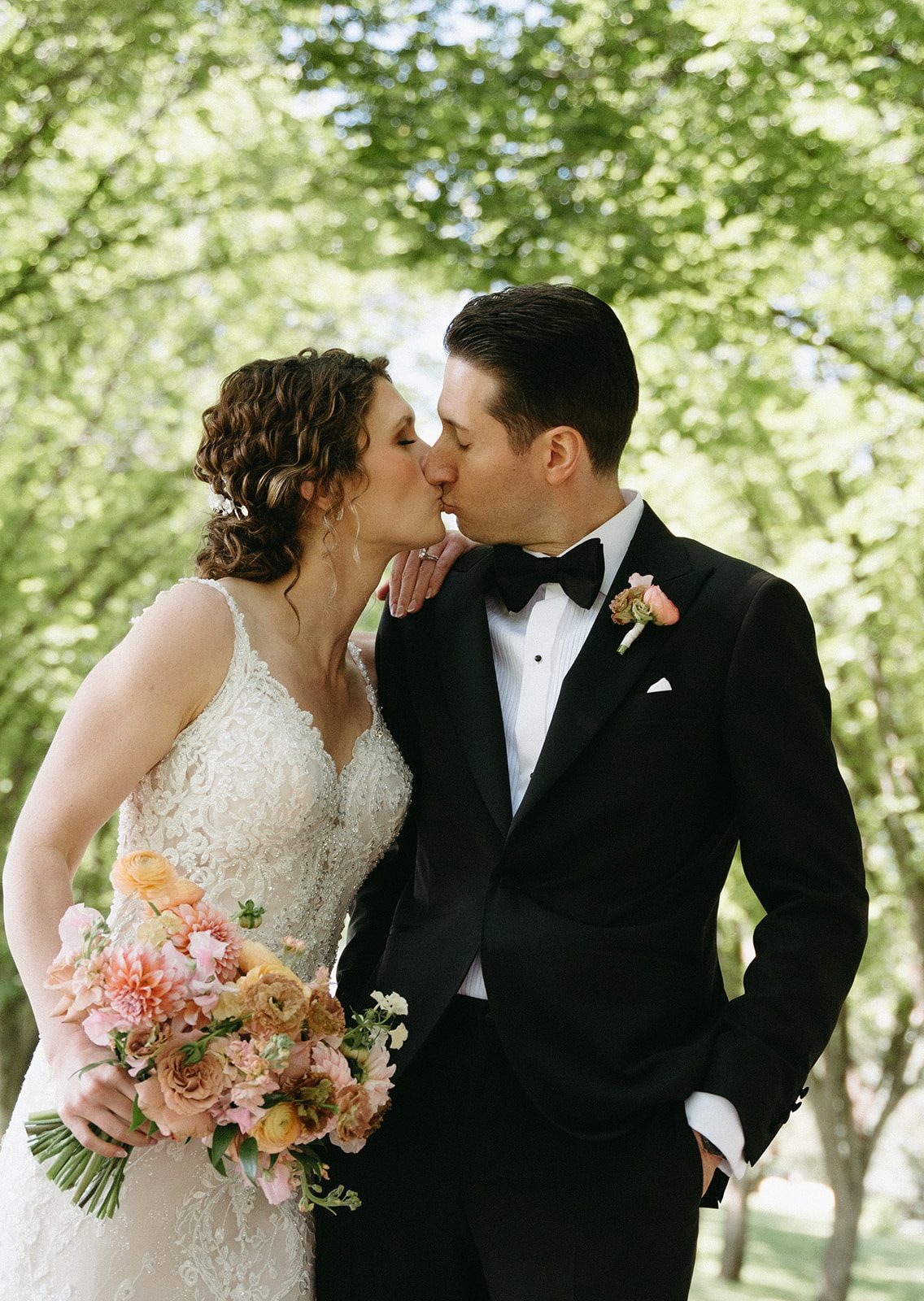 Bride and groom share a kiss while she is holding her pink and peach garden inspired bridal bouquet.