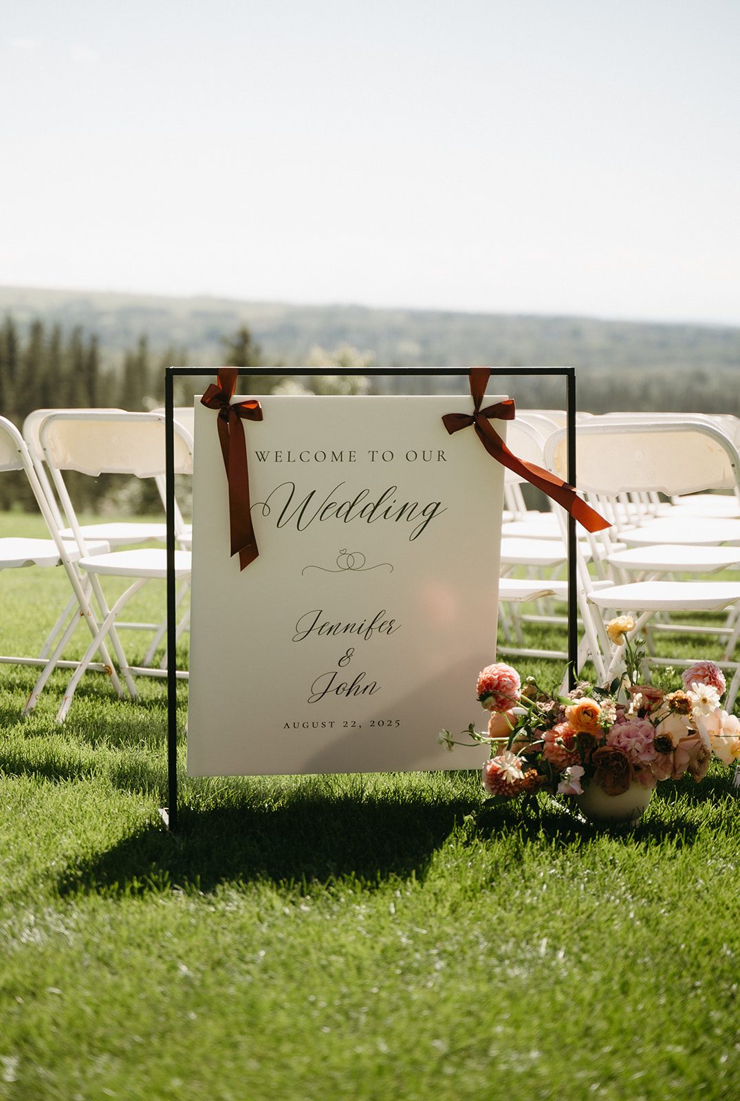 A welcome sign with a garden inspired pink and peach arrangement at its base at the start of the aisle.