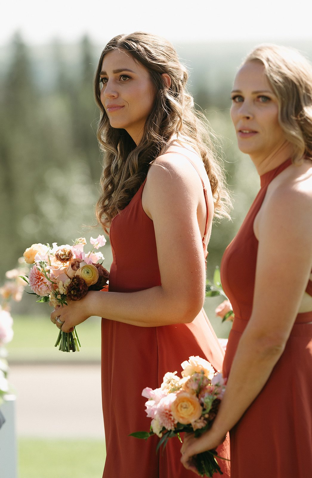 Bridesmaids in full length terracotta gowns holding pink and peach garden inspired bouquets turn their heads to watch the bride come down the aisle.