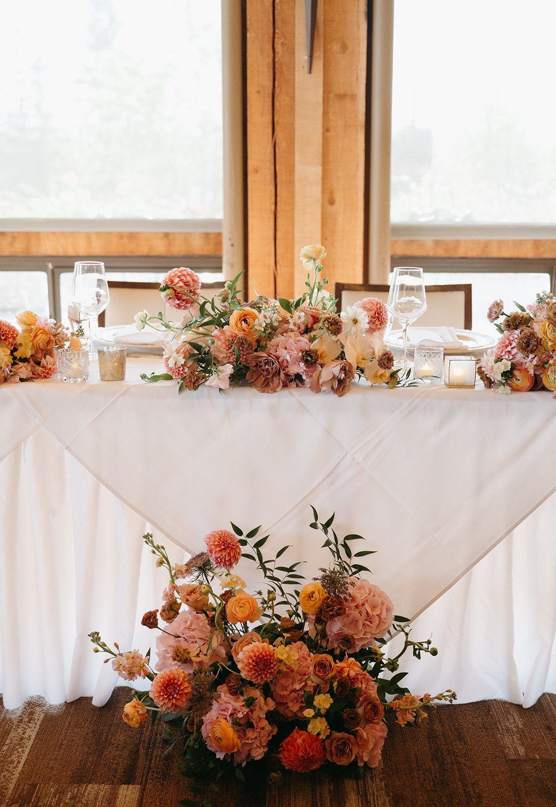 Cluster of three pink and peach garden inspired floral arrangements on the head table, with a larger one on the floor in front of the table.