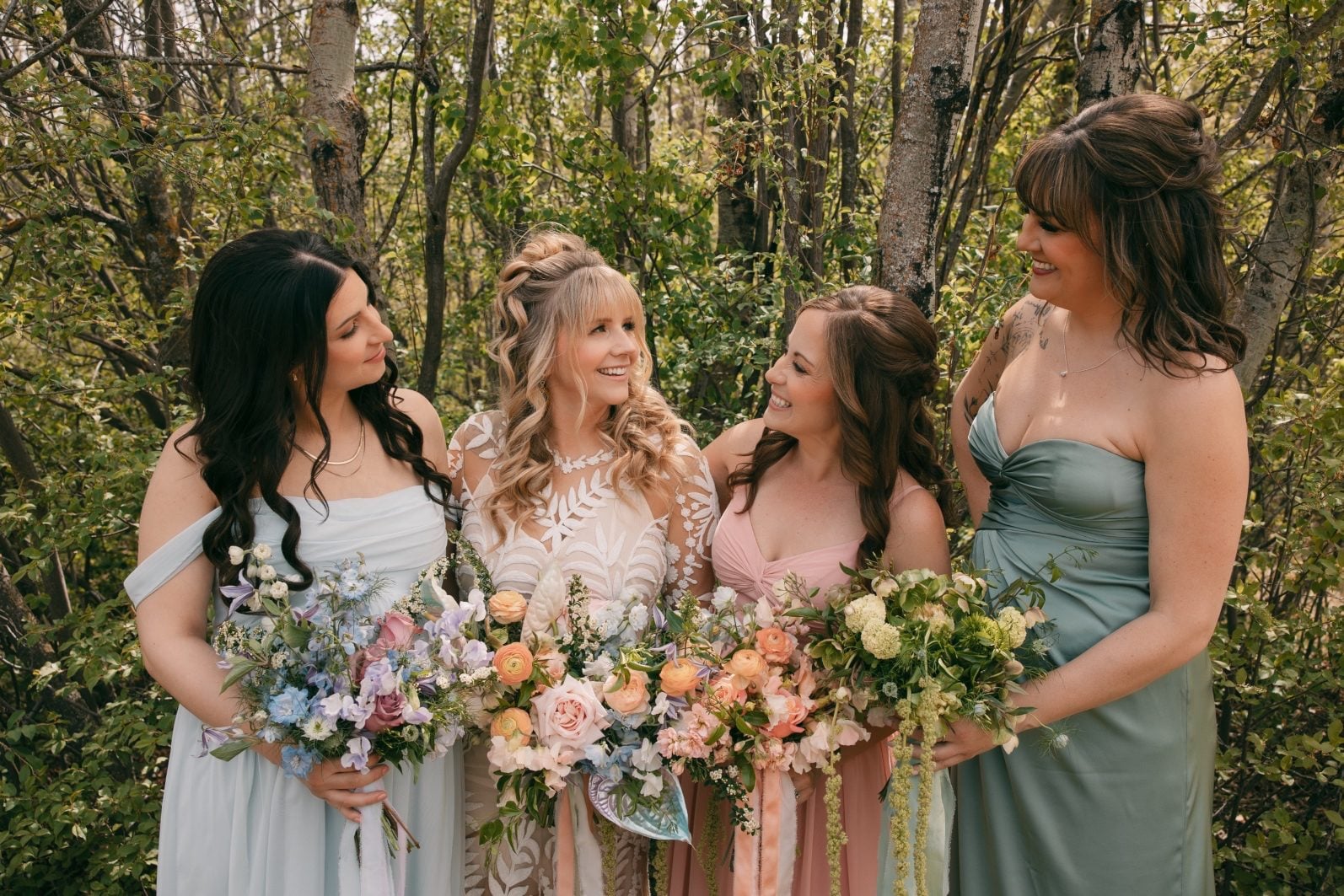 Bride and bridesmaids carrying colourful bouquets designed to complement their blue, green and pink dresses.