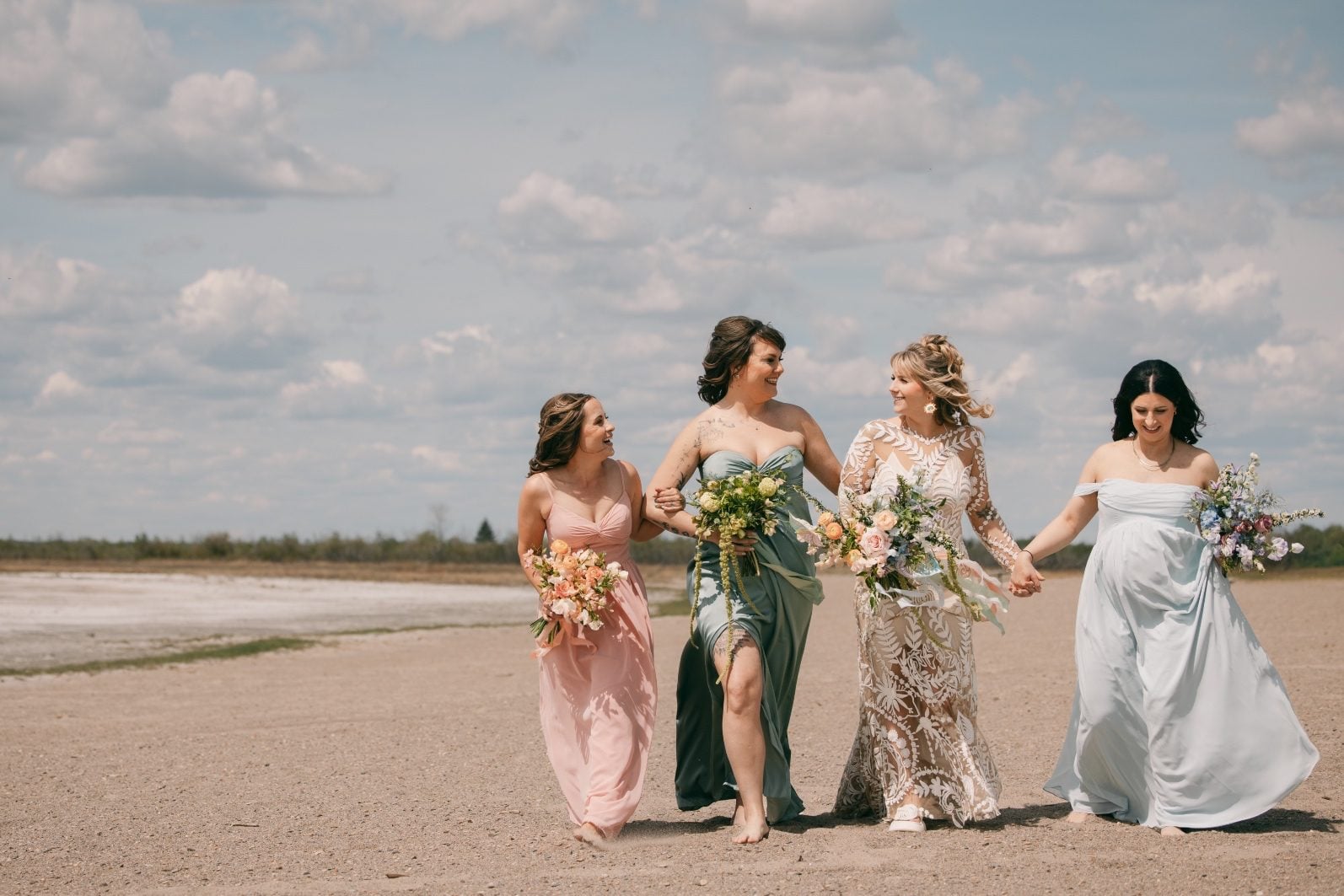 Bride and bridesmaids walking together with a rainbow ombre wedding flowers, their pastel bouquets to match their dress colour.