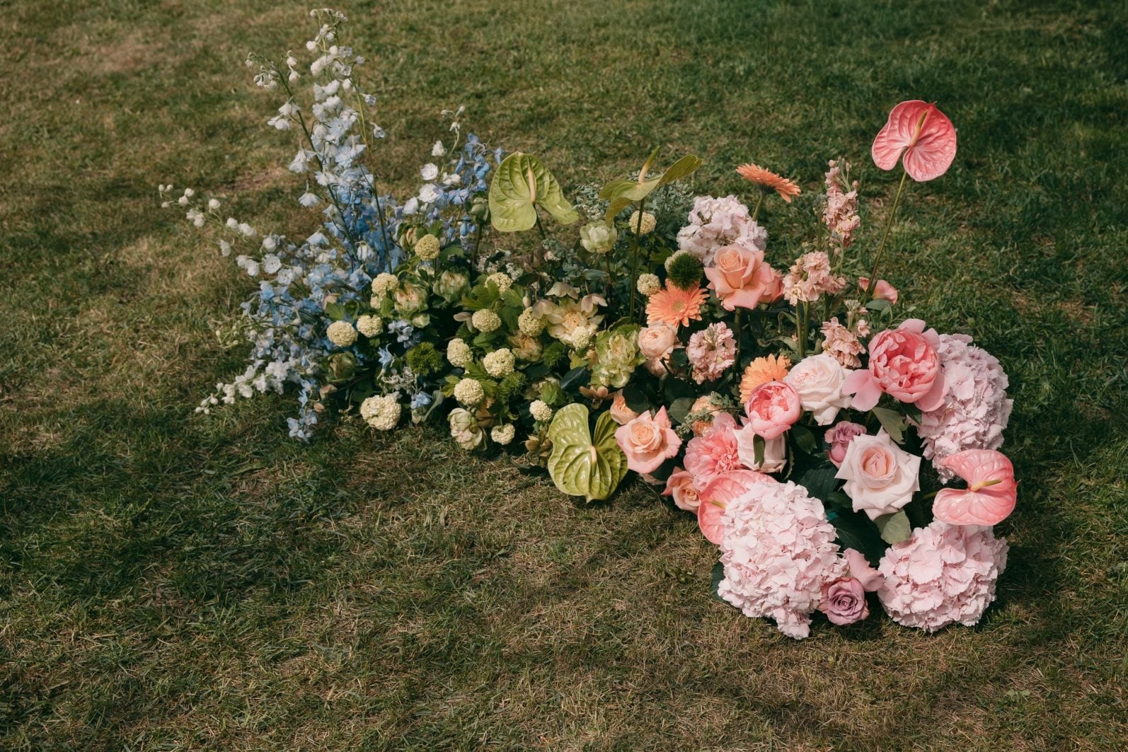 Ground floral installation transitioning from blue and green into pink and peach for a pastel rainbow wedding ceremony.