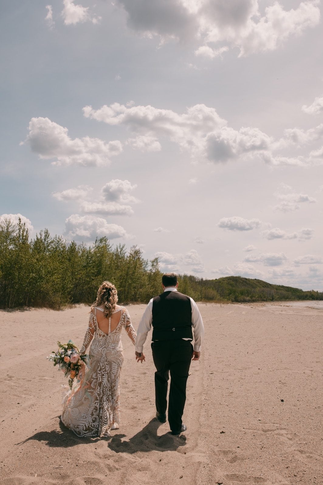 Bride and groom walking hand in hand across the natural landscape with her colourful rainbow ombre bouquet.