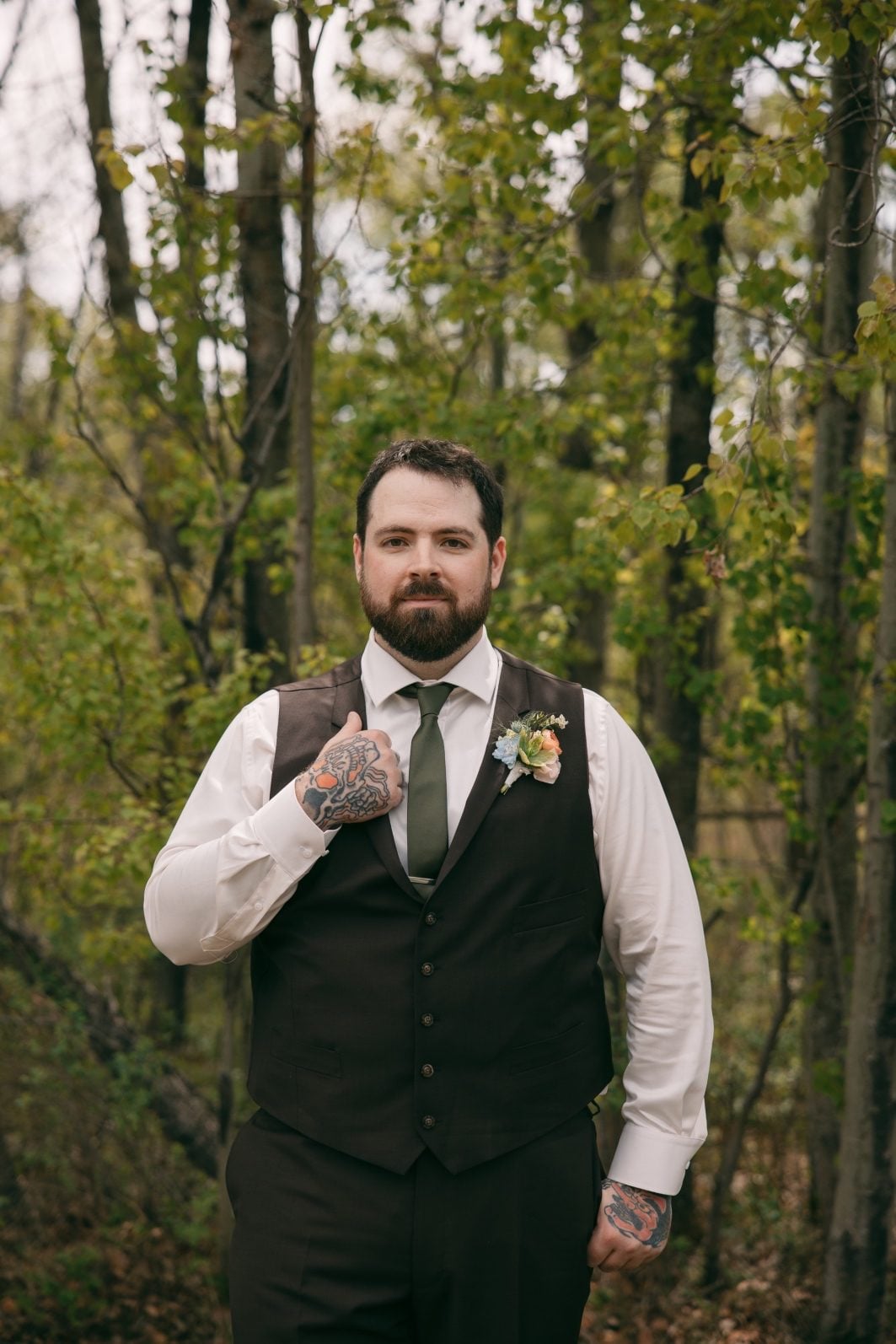 Groom wearing a colourful peach, blue and green floral boutonnière at an outdoor wedding.