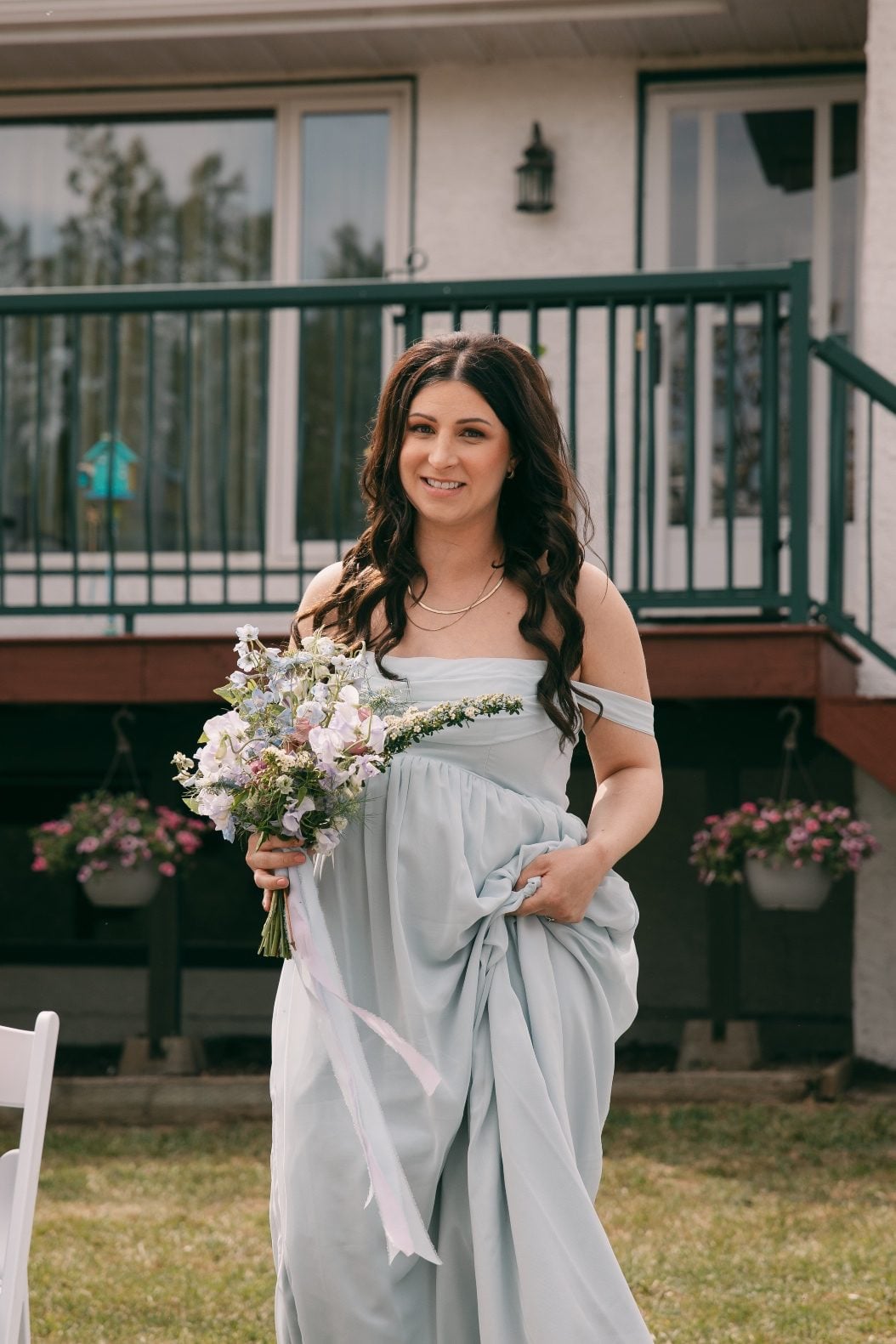 Bridesmaid in a pale blue dress carrying a loose garden style bouquet of soft blue, lavender and white flowers.