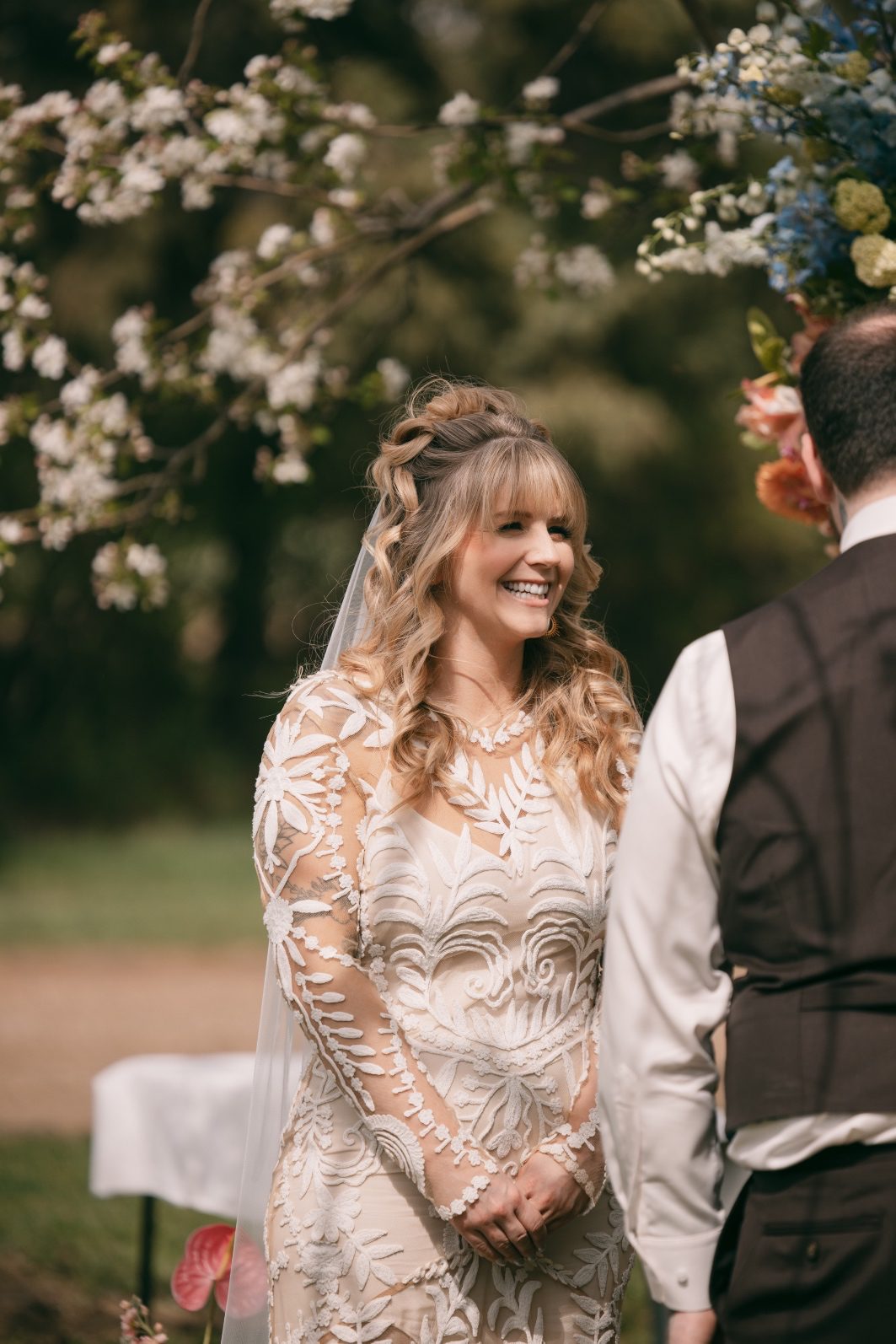 Smiling bride in a detailed lace wedding dress during her colourful outdoor spring ceremony.