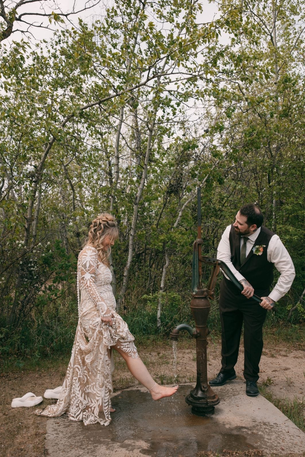 Bride and groom sharing a playful moment beside a vintage water pump at the Buffalo Lake Campground.