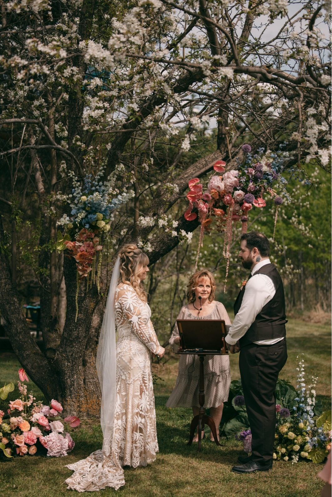 Bride and groom exchanging vows beneath a flower tree decorated with cascading pastel wedding flowers.