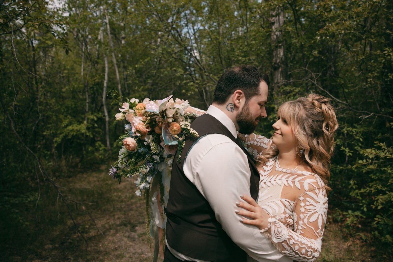 Bride and groom embracing in the woods with her rainbow ombre bridal bouquet.