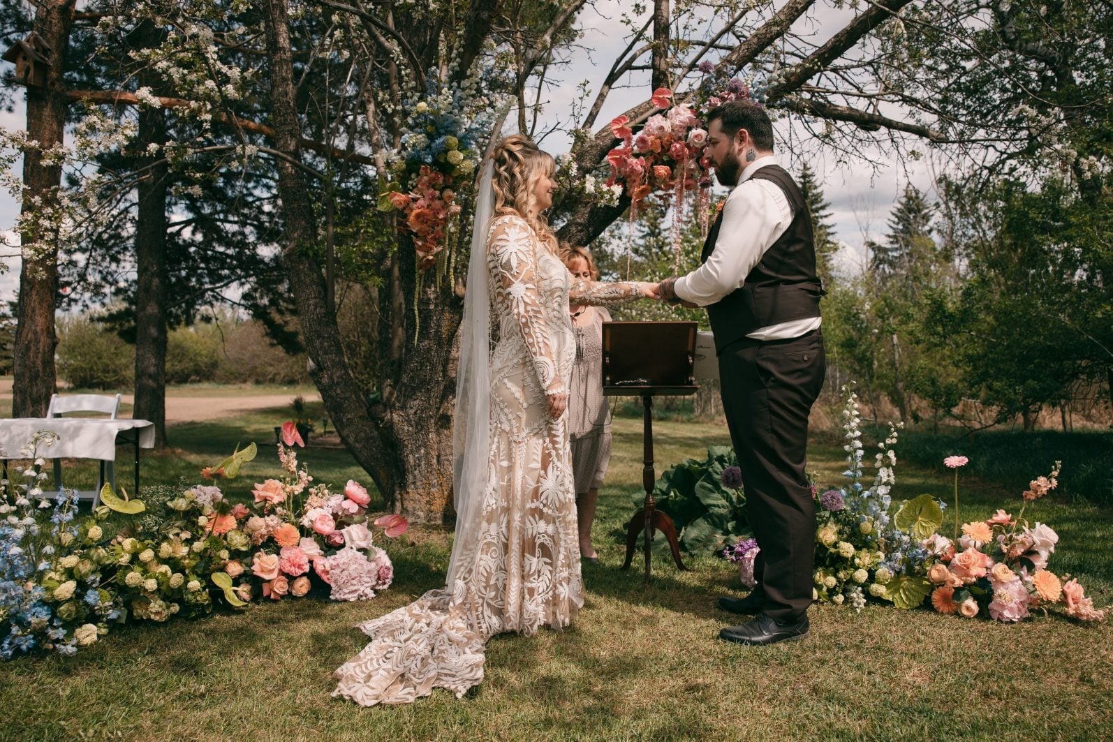 Bride and groom exchanging rings surrounded by colour blocked ground florals in blue, green, peach, pink and purple.
