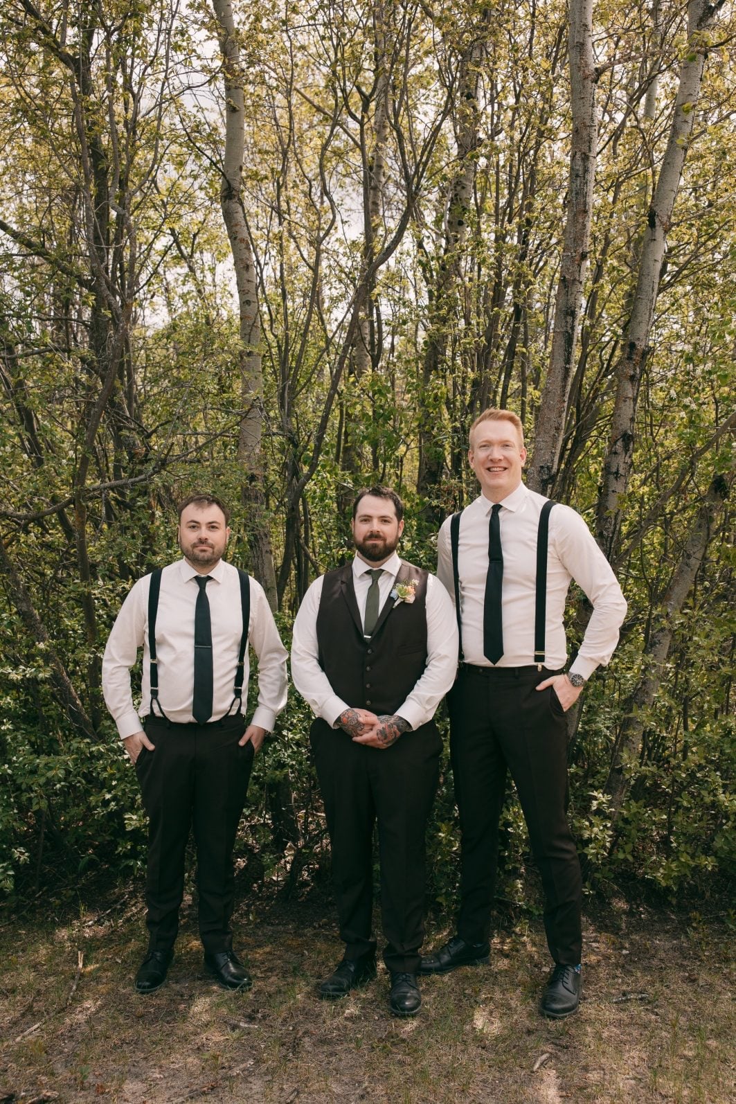 Groom and groomsmen in black and white wedding attire posing together among the trees.