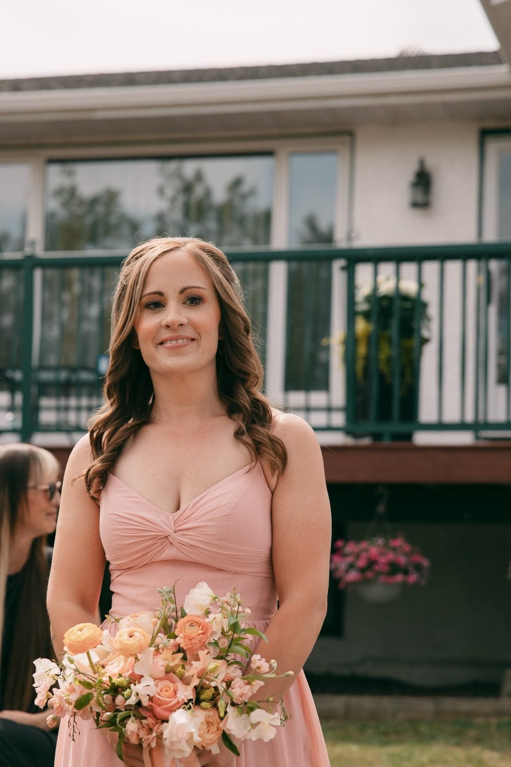 Bridesmaid in a blush pink dress carrying a peach and pink spring bouquet with ranunculus, roses and sweet peas.