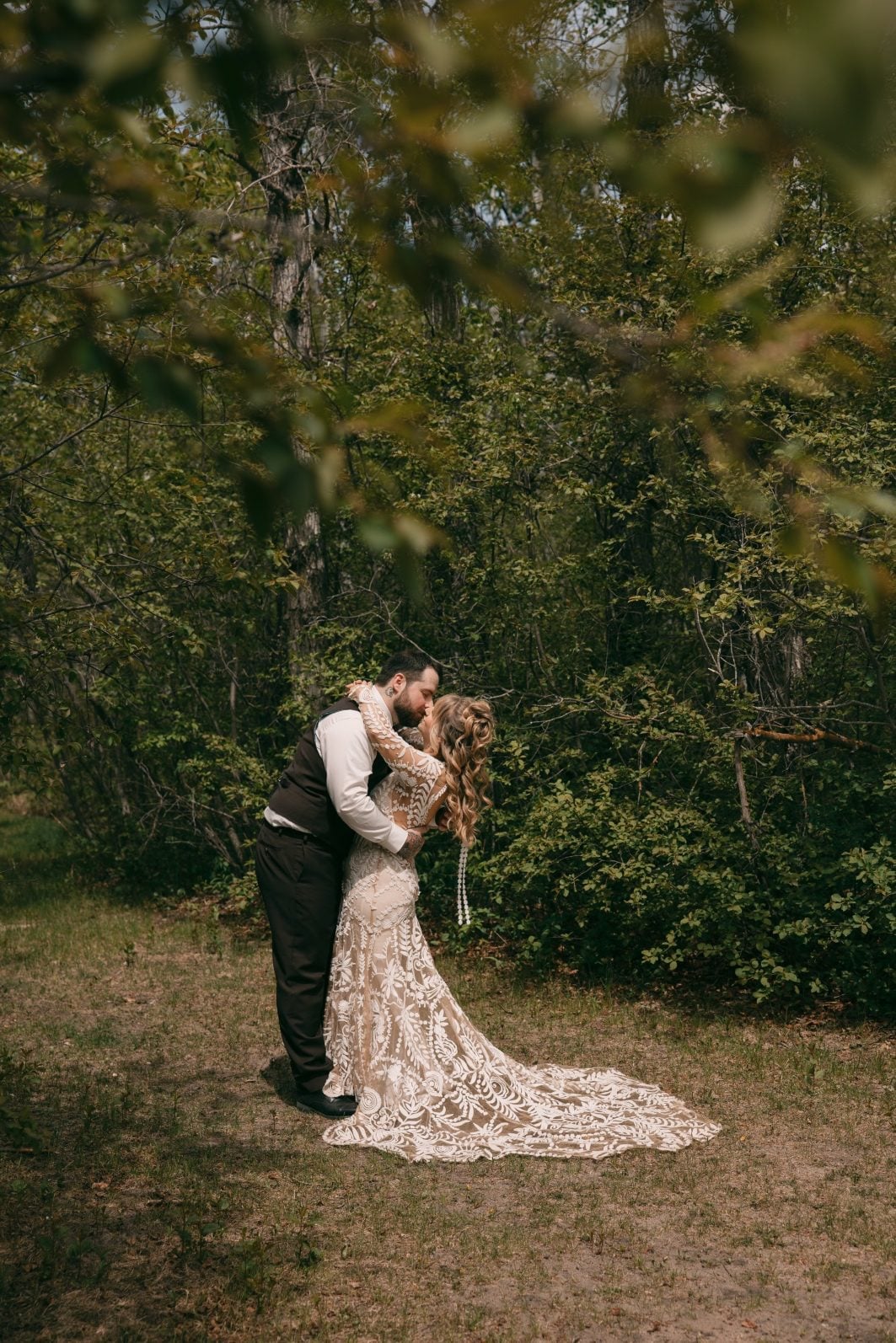 Bride and groom sharing a kiss among the trees.