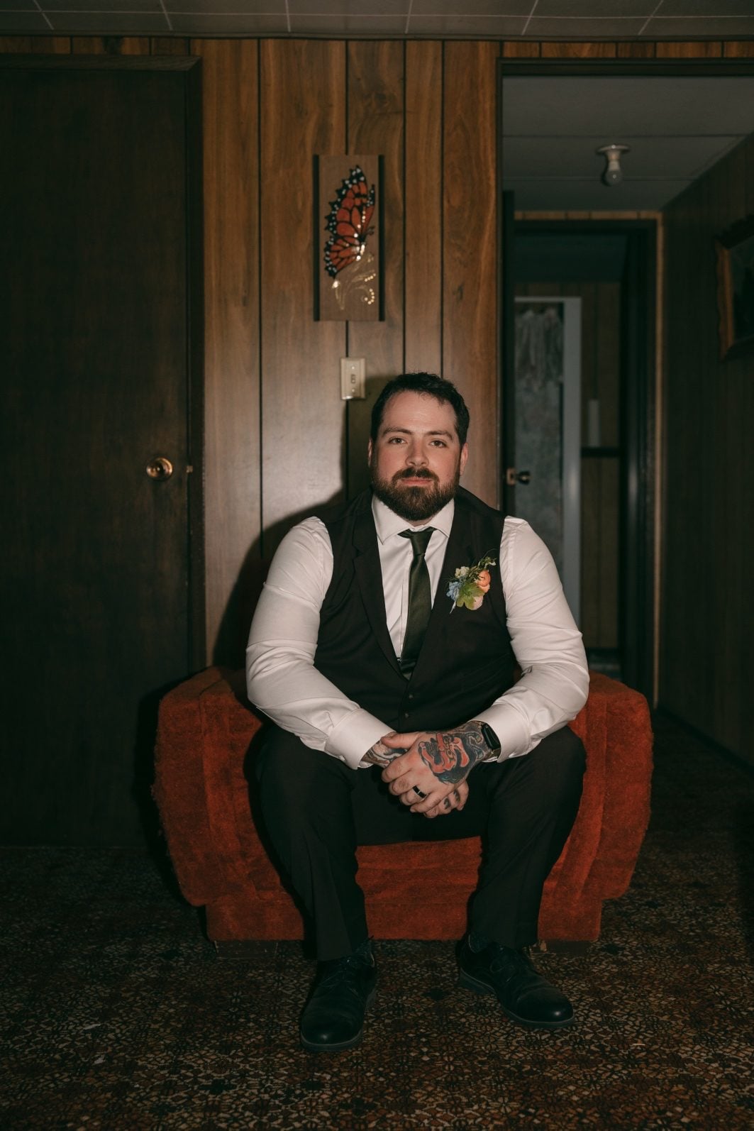 Groom seated in a vintage orange chair wearing a colourful pastel floral boutonnière.