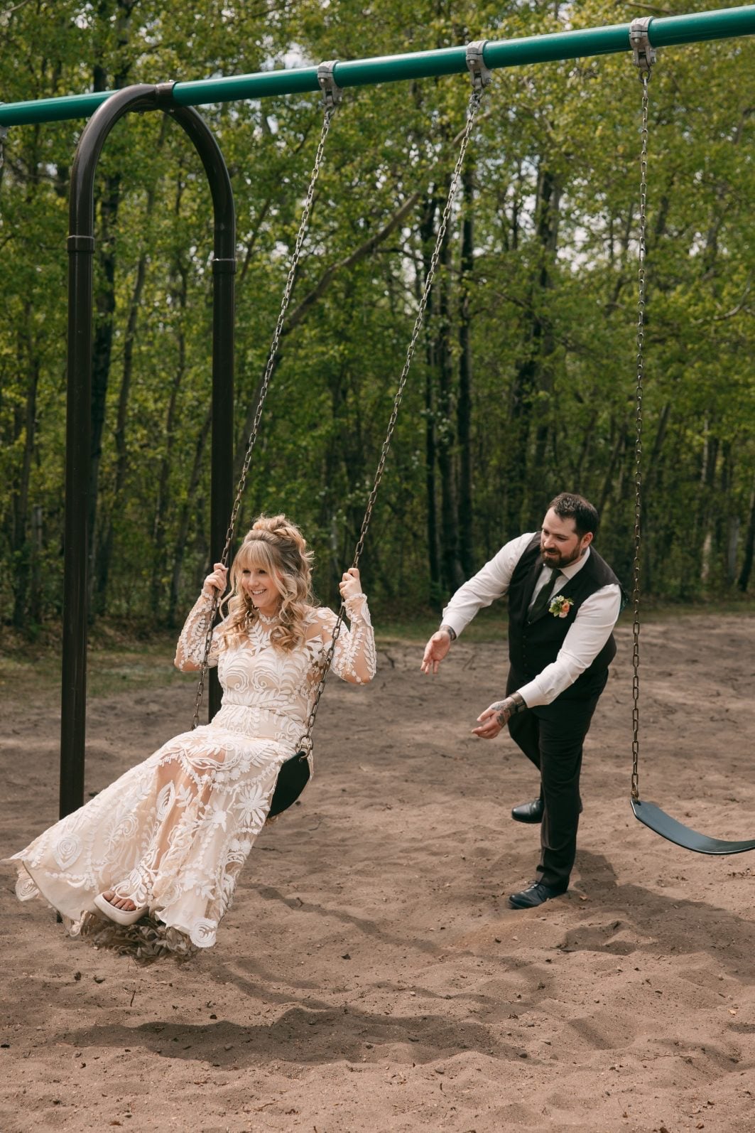 Groom playfully pushing the bride on a swing during their relaxed outdoor wedding portraits at Buffalo Lake Campground.