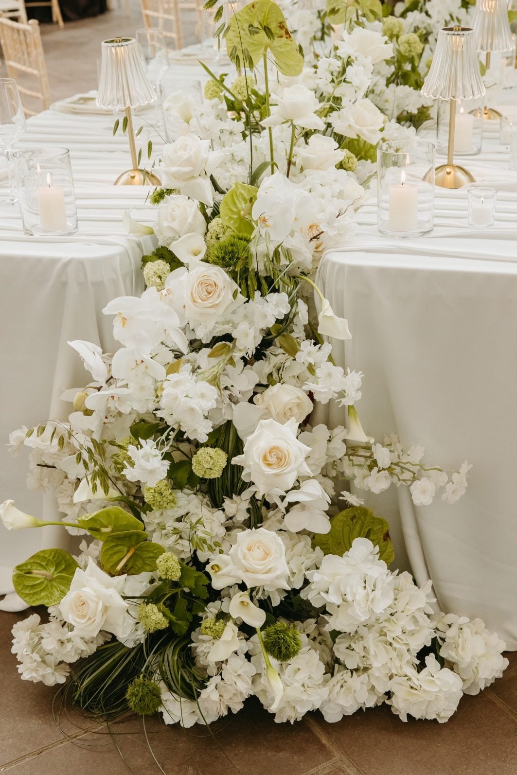 White and Green Floral Waterfall White and green wedding flowers cascading down the front of the large feature table including hydrangea, roses, anthurium, viburnum, callas, dianthus and decorative grasses.