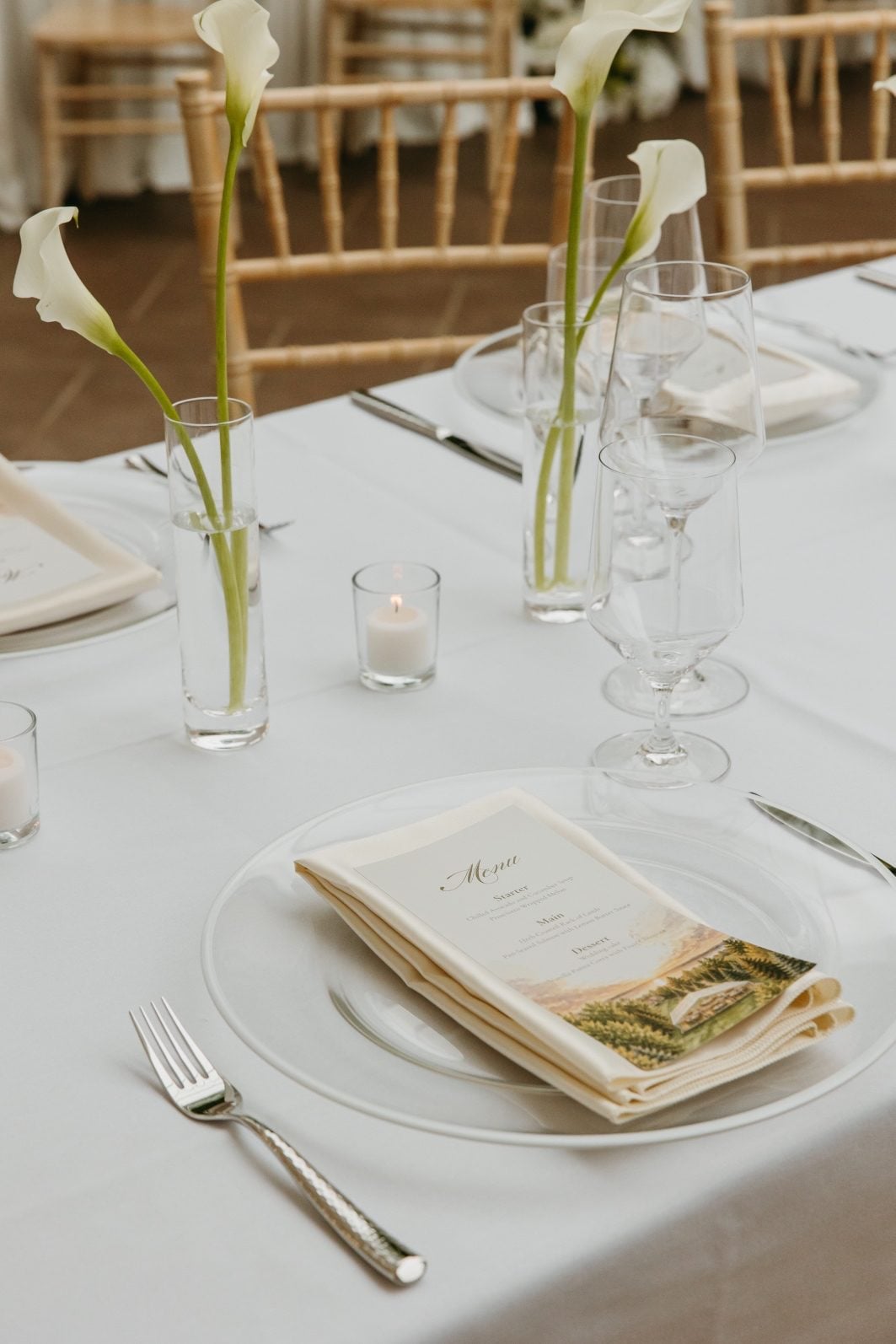 White and Green Wedding Flowers Callas White and green wedding flower place setting with glass charger plate, ivory napkins, decorative menu, white calla bud vases accented with little votive candles in between.