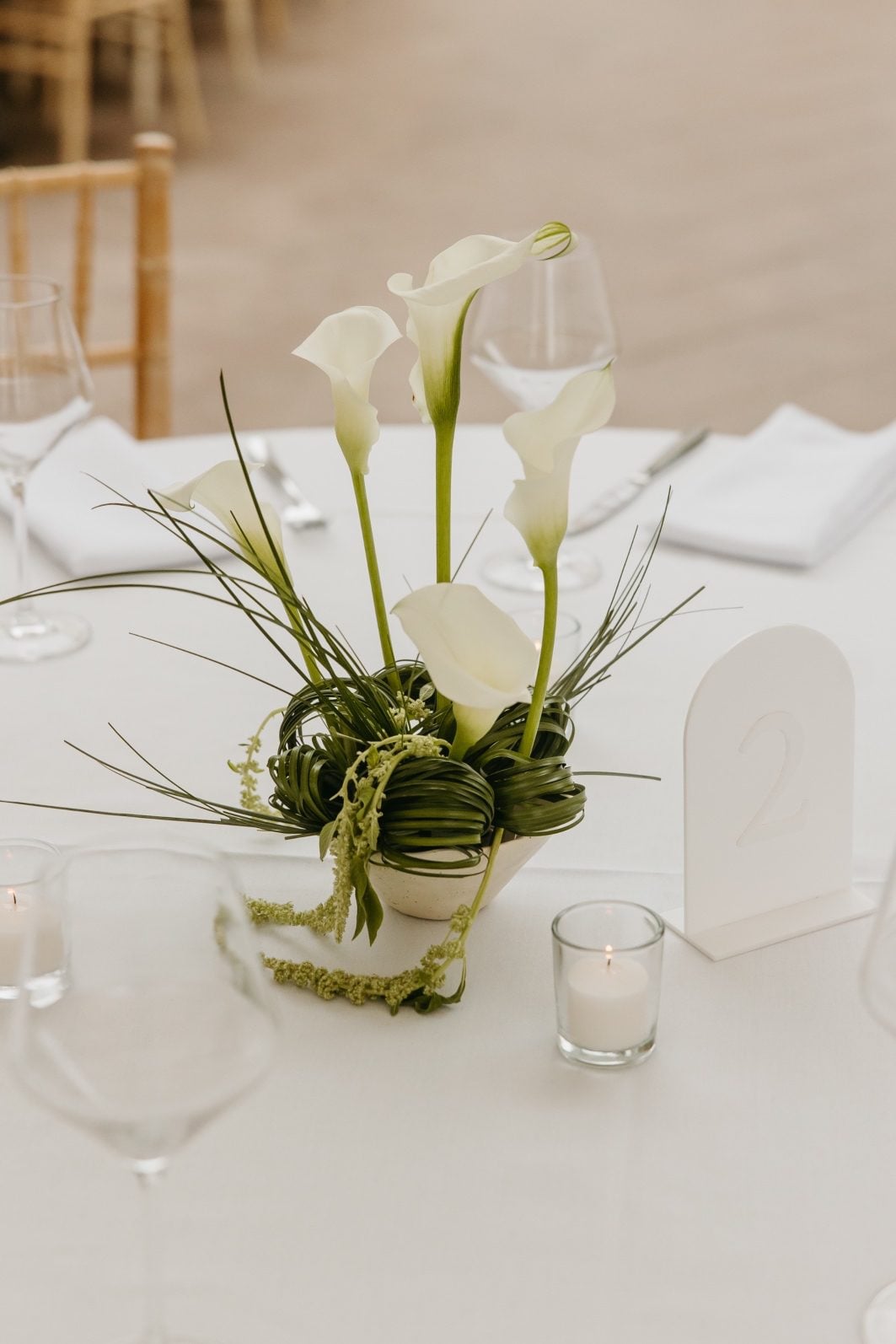 White and Green Wedding Flowers Centrepiece Close up of stunning, sculptural green and white ikebana inspired centrepiece featuring white calla lilies, sculptural loops of bear grass and green hanging amaranths.