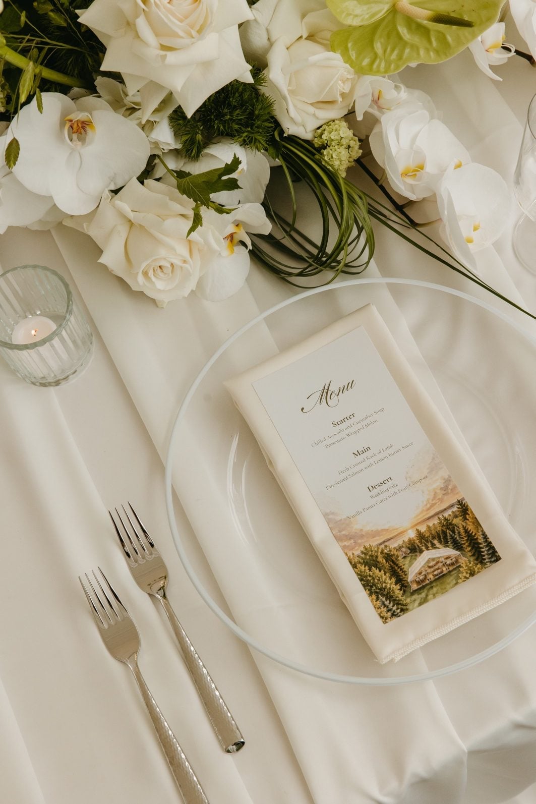 White and Green Wedding Flowers Place Setting Place setting at the featured table showcasing the menu carts with a portion of the floral waterfall showing at the top, with orchids, roses and loops of bear grass against the layers of the soft ivory satin tablecloth.