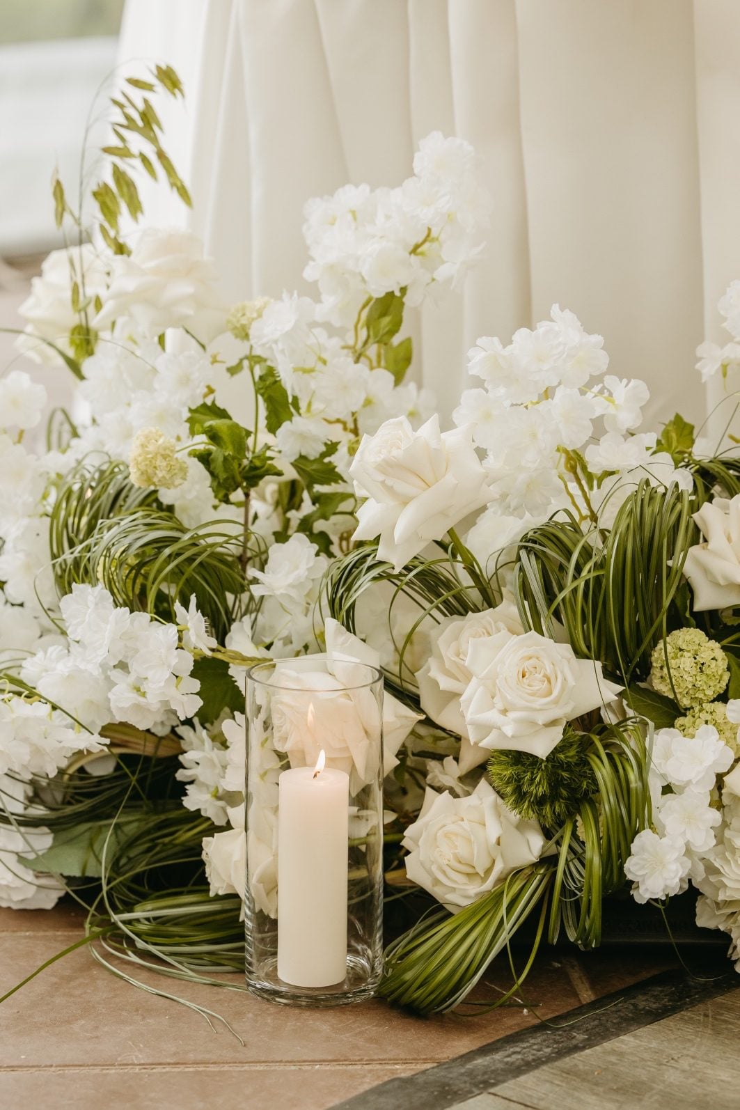 White and Green Wedding Flowers Fresh white and green wedding flowers arranged in front of the sweetheart table accented by ivory pillar candles in cylinder vases.
