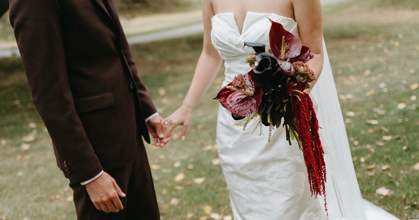 A+J Structural Bridal Bouquet Andi and Logan holding hands, while she holds her structural bridal bouquet in the other hand, in a mixture of red and burgundy with anthurium and amaranthus.