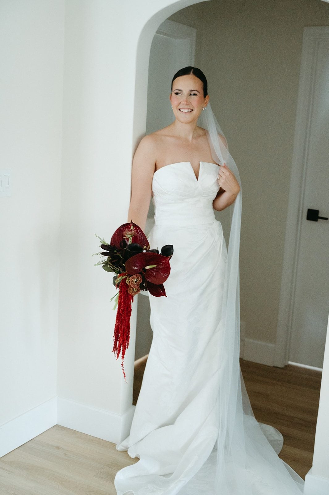 Andi + Logan Bride holding a rich burgundy sculptural wedding bouquet with anthurium, calla lilies and cascading red amaranthus.