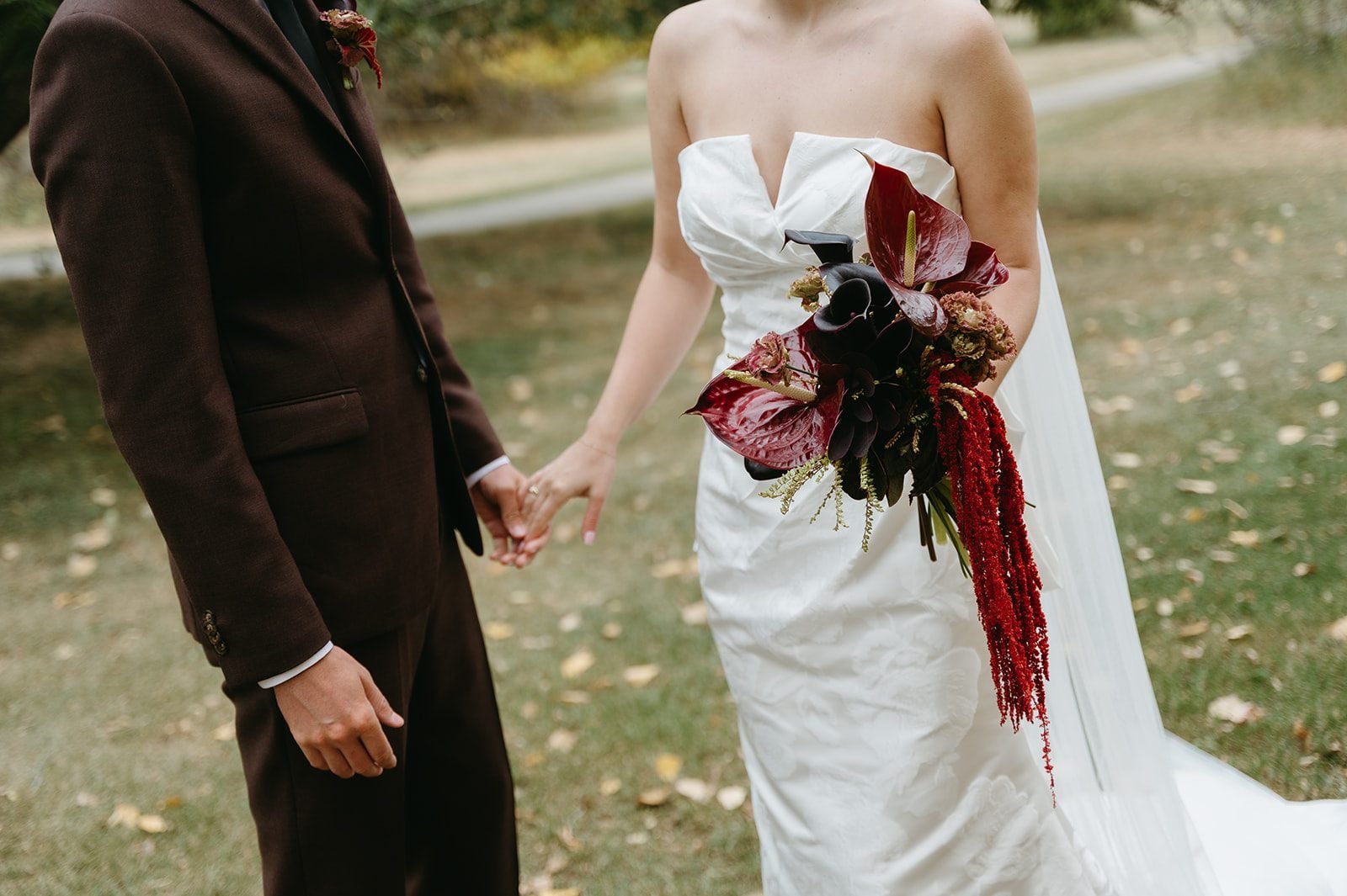 Andi + Logan Fall bride and groom holding hands besides a dramatic burgundy bouquet with sculptural anthurium and cascading amaranthus.