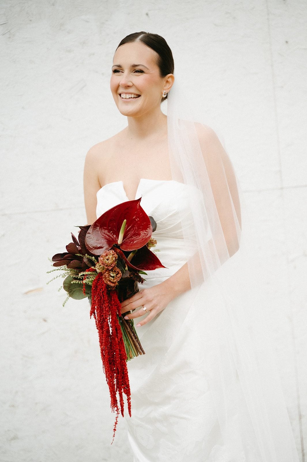 Andi + Logan Bride holding sculptural wedding flowers in deep burgundy and red against her modern white wedding gown.