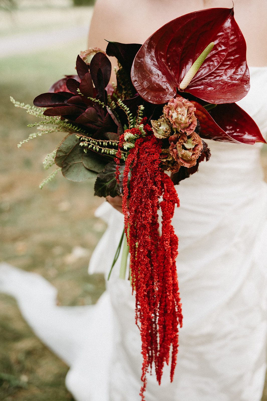 Andi + Logan Close up of a sculptural bridal bouquet with burgundy anthurium, dark foliage, textural blooms and cascading red amaranthus.